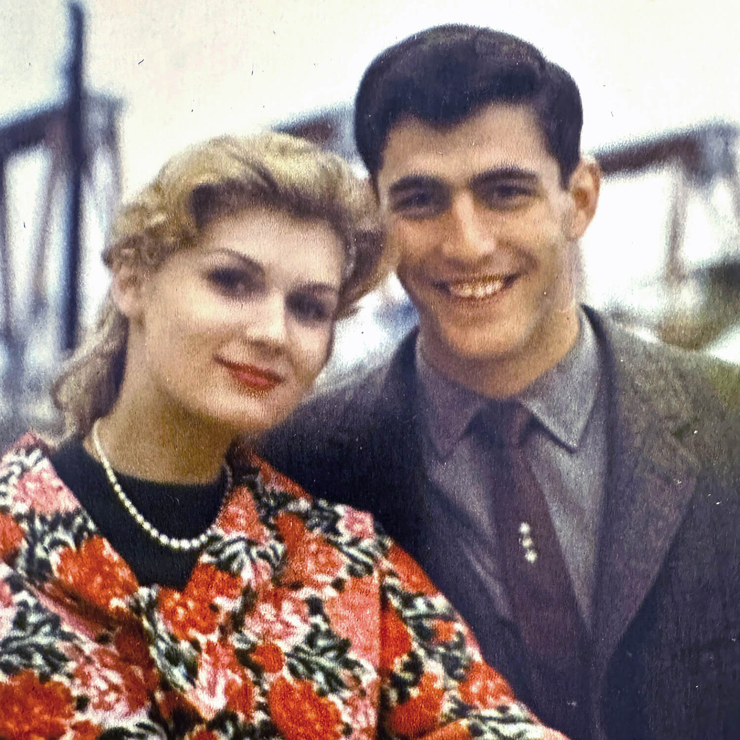 Sally Gordon, wearing a red floral jacket, stands to the left of her husband Michael in 1961, as he holds her right hand with his right hand.