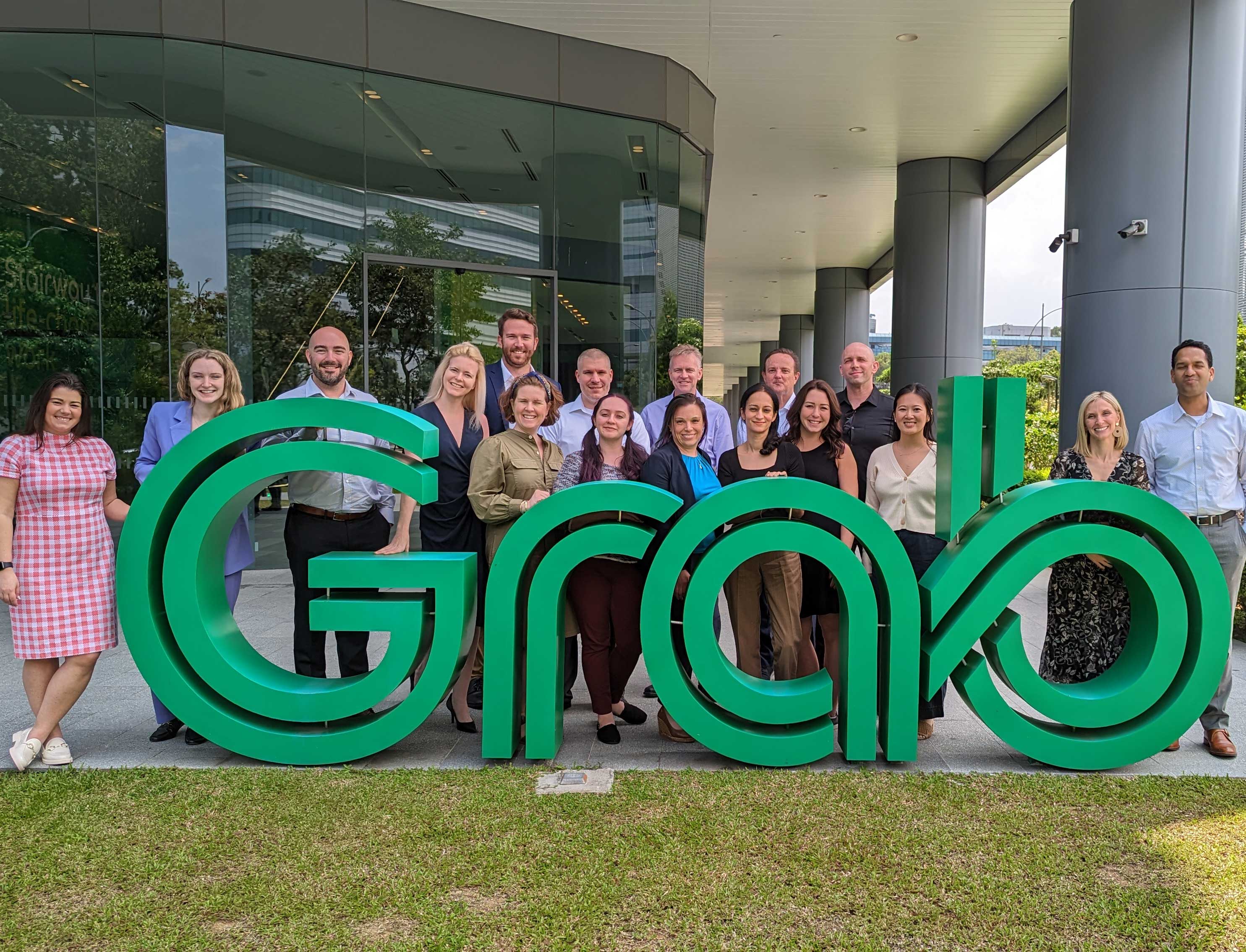 A group of FLEX MBA students pose together outside of Grab headquarters in Singapore. They stand behind a large 'grab' sign.
