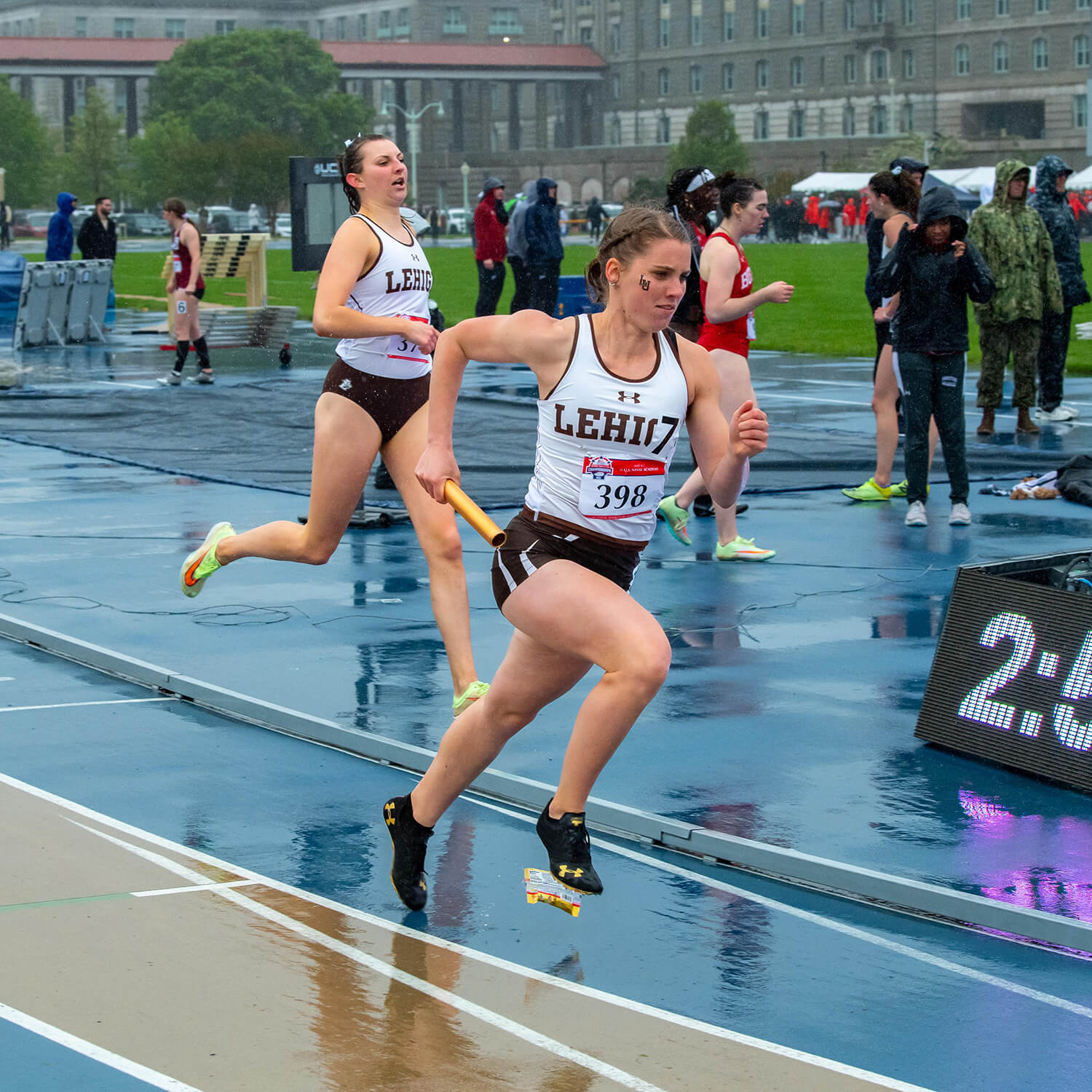 Wearing a Lehigh track uniform, Kaja Skerlj races in the rain on a track with a baton in her hand.