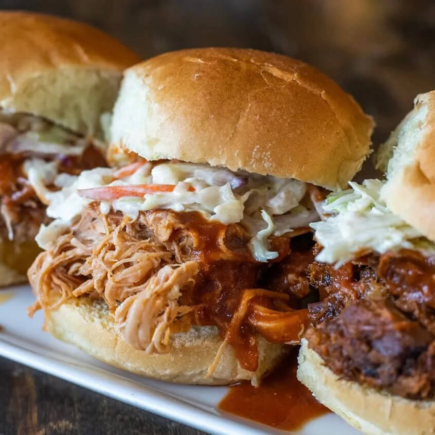 Close-up of three pulled pork sliders with coleslaw and sauce on a white plate