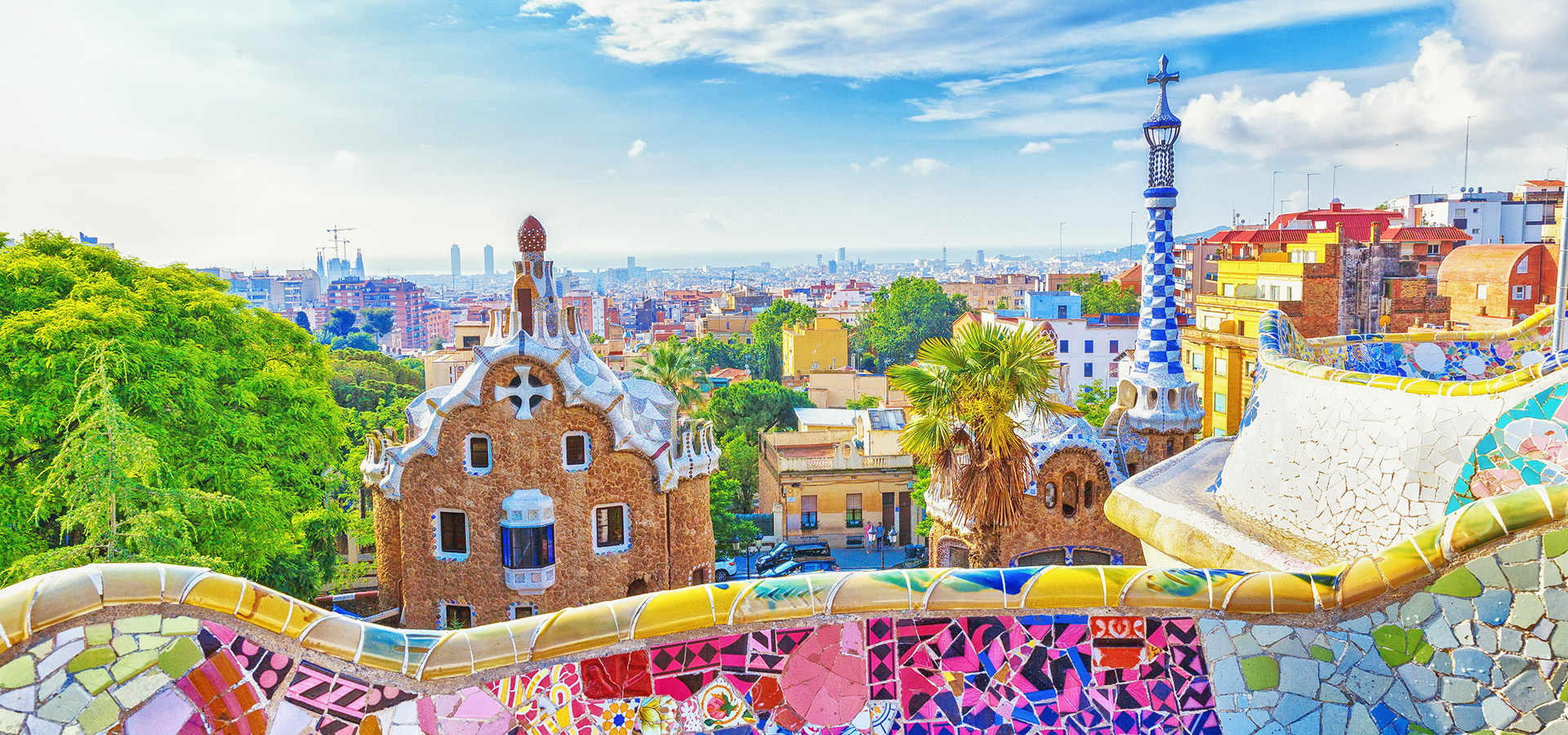 The colorful stone and mosaic railing of Park Güell, overlooking buildings in Barcelona.