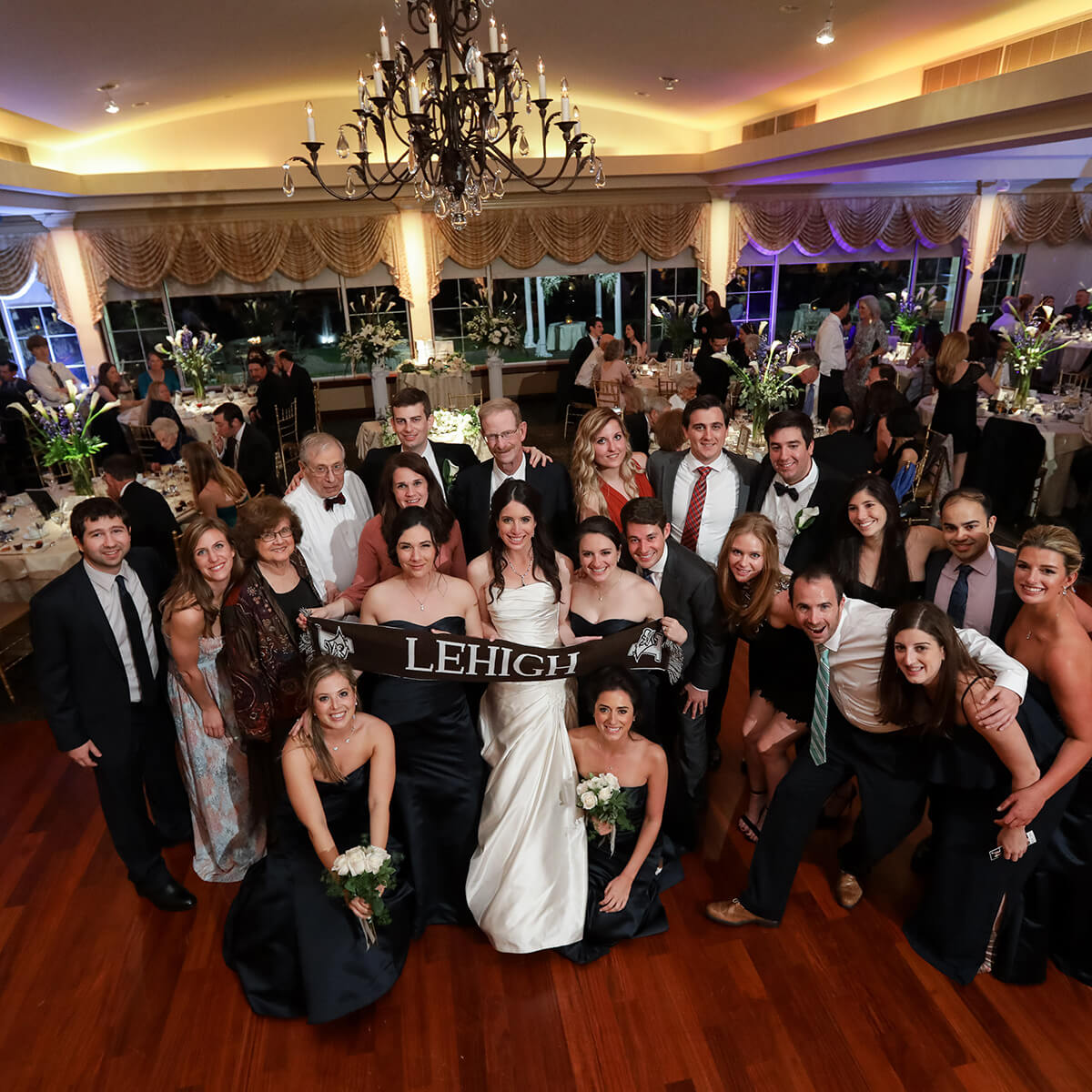 A bridal party and guests holding a brown Lehigh banner pose for a photo taken from above.