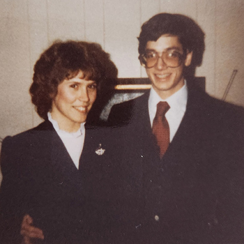 A young couple in 1980s business suits smile big