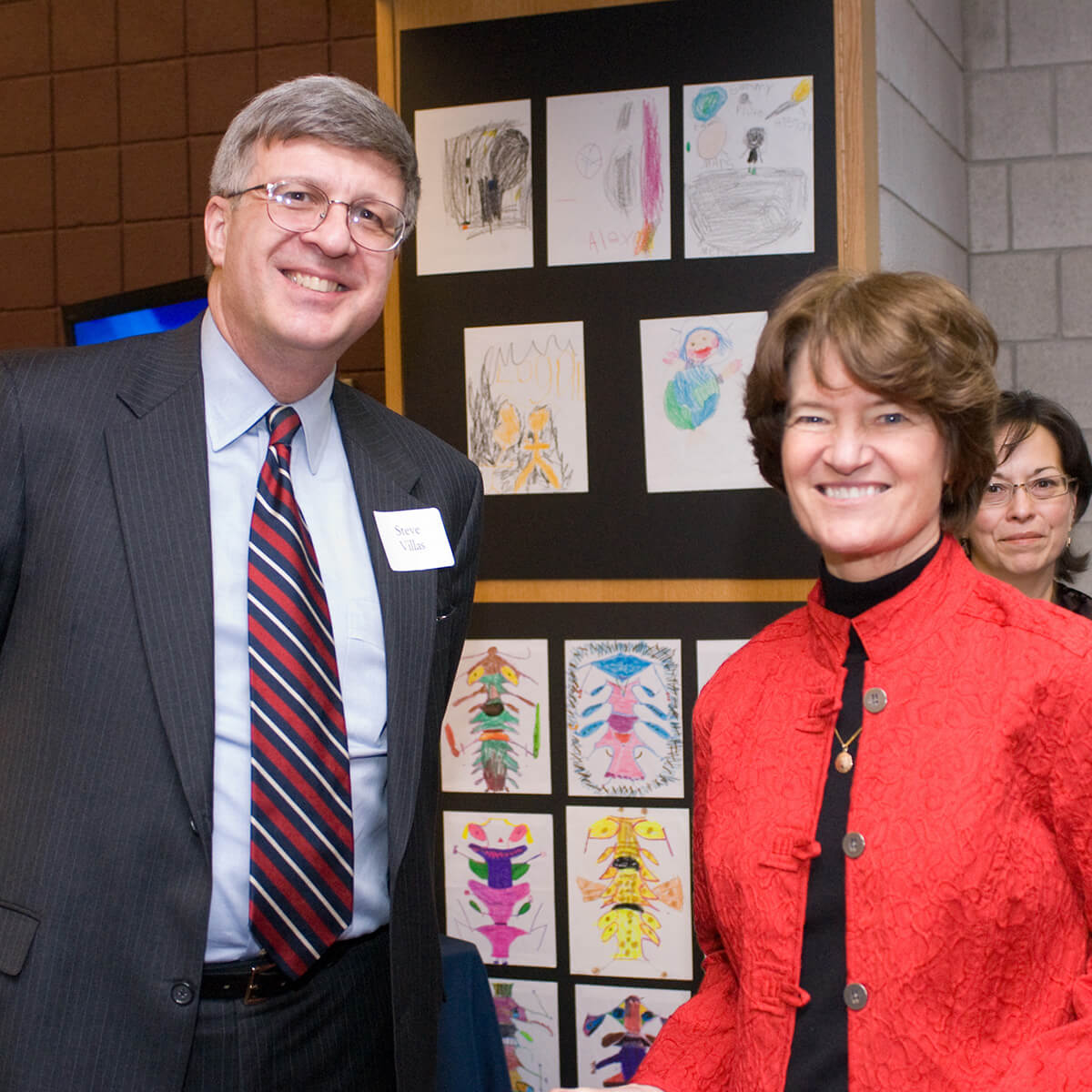 Steve Villas stands wearing a suit and tie beside Sally Ride, wearing a red jacket over a black turtleneck.