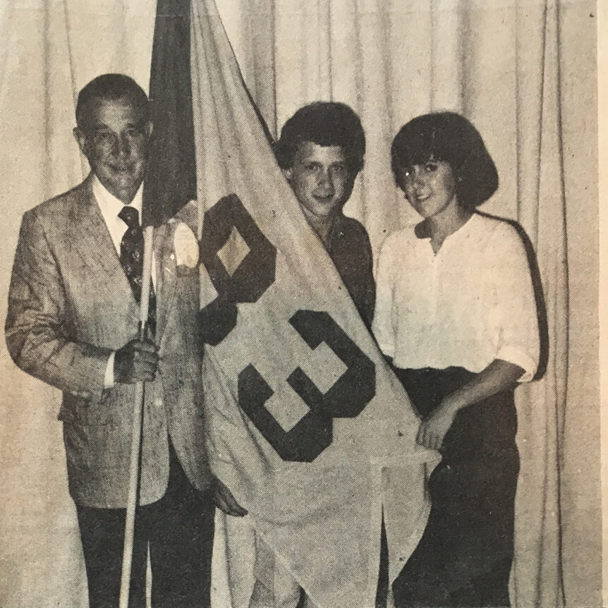 A man and two college students holding a Class of 1983 flag