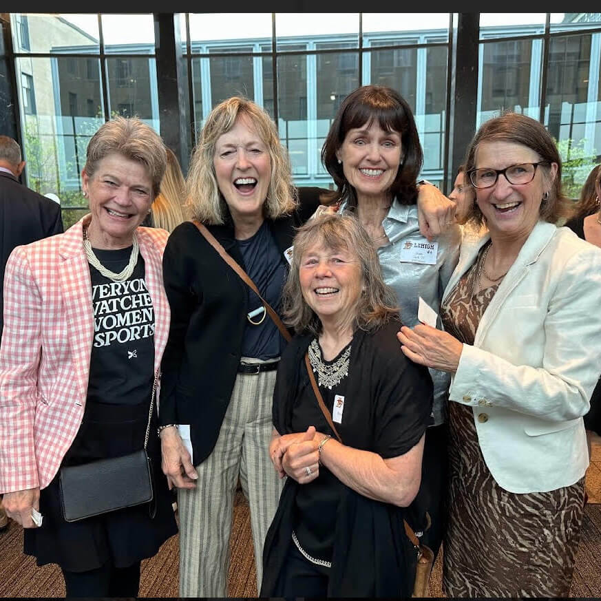 Sue Sachs stands with four other women, all wearing gleeful smiles and delightfully posing with their arms wrapped around each other’s shoulders.