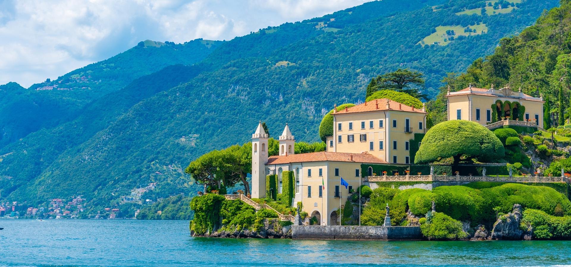 A building sits on the edge of the water, surrounded by greenery.