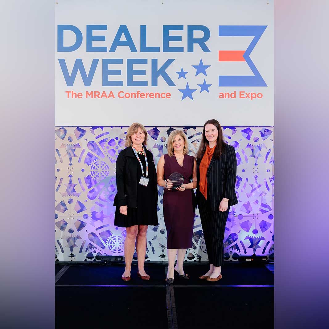 Taylor and two colleagues pose in business attire at a conference and hold an award.
