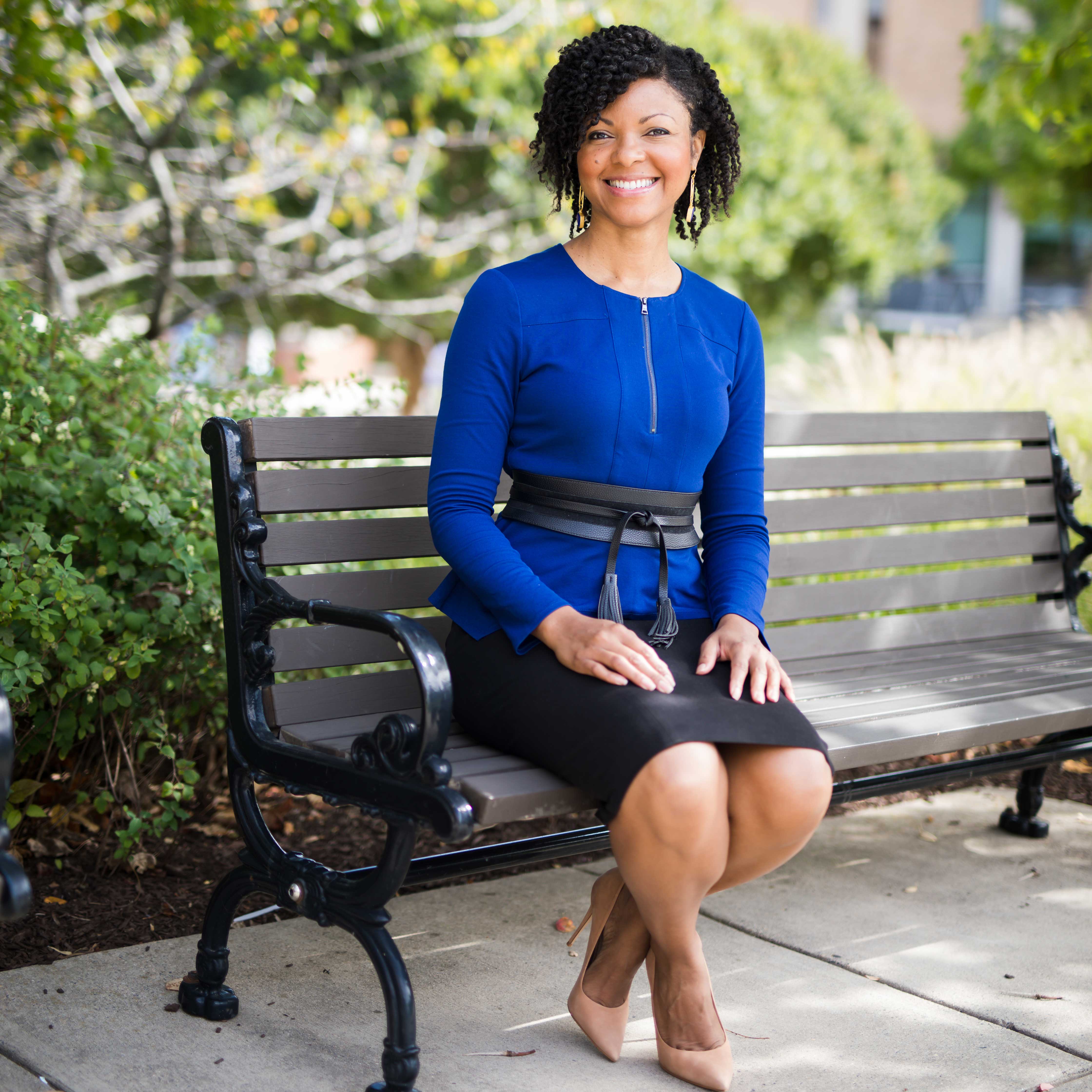 Terry-Ann Jones wears a blue top and black skirt while sitting on a bench on campus.