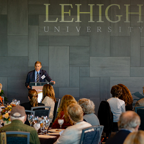 Kevin Clayton leans on a podium with a Lehigh logo behind him