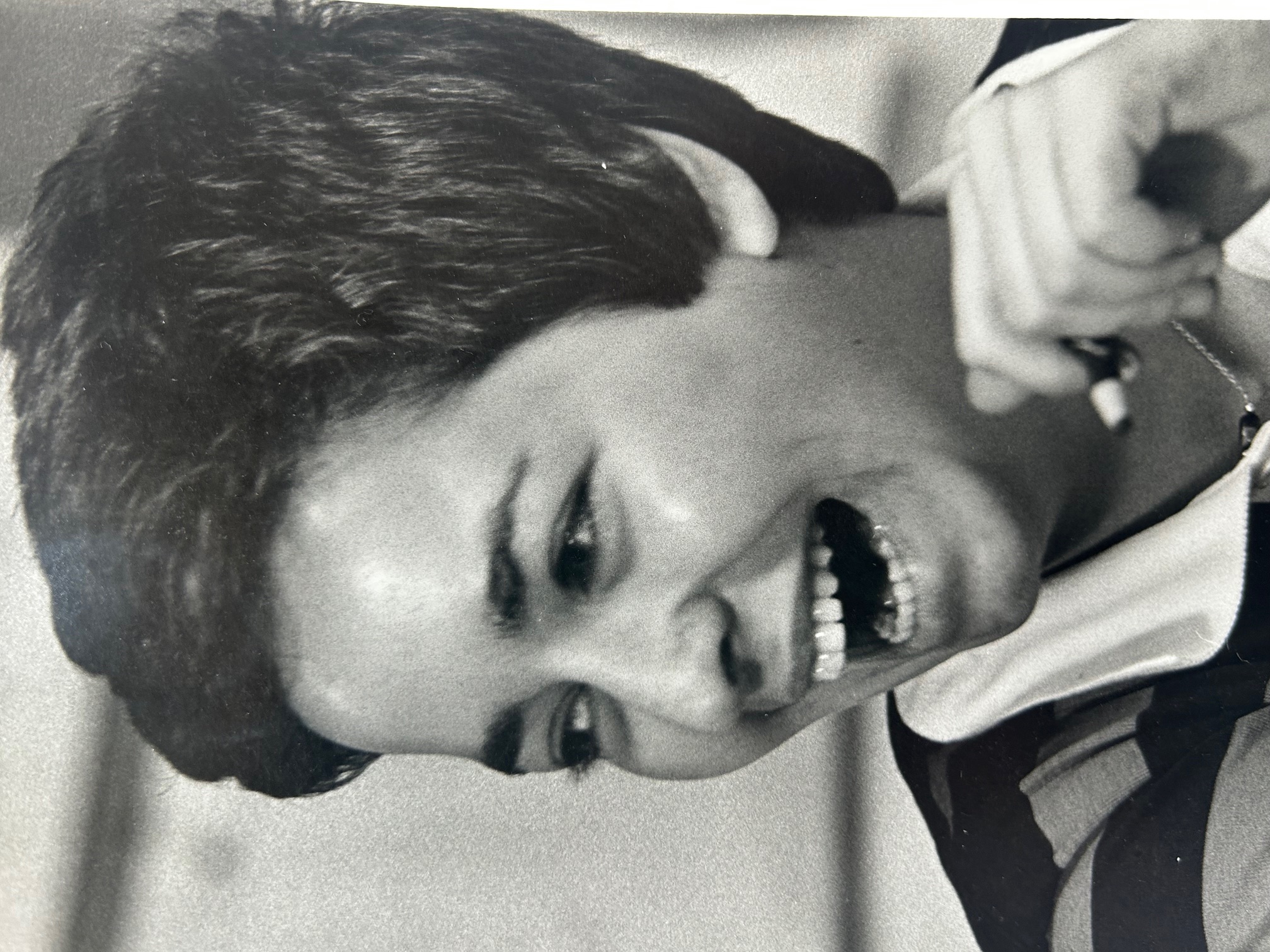 A black-and-white photo of Louise; the looks off to the left and smiles while holding a pen in her raised hand.