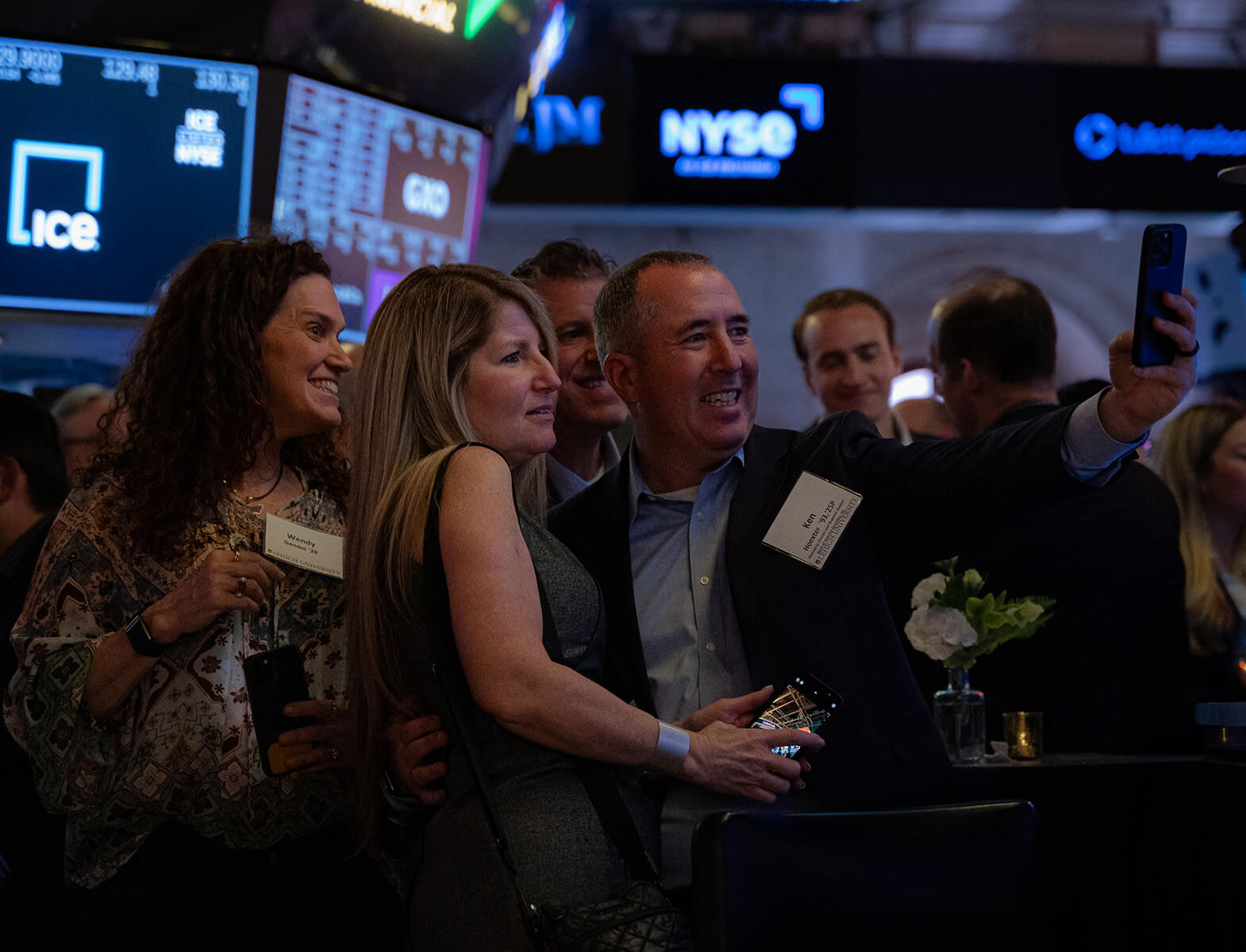 Ken Hoexter poses for a selfie with fellow alumni at the New York Stock Exchange,, with his arm outstretched holding his phone.