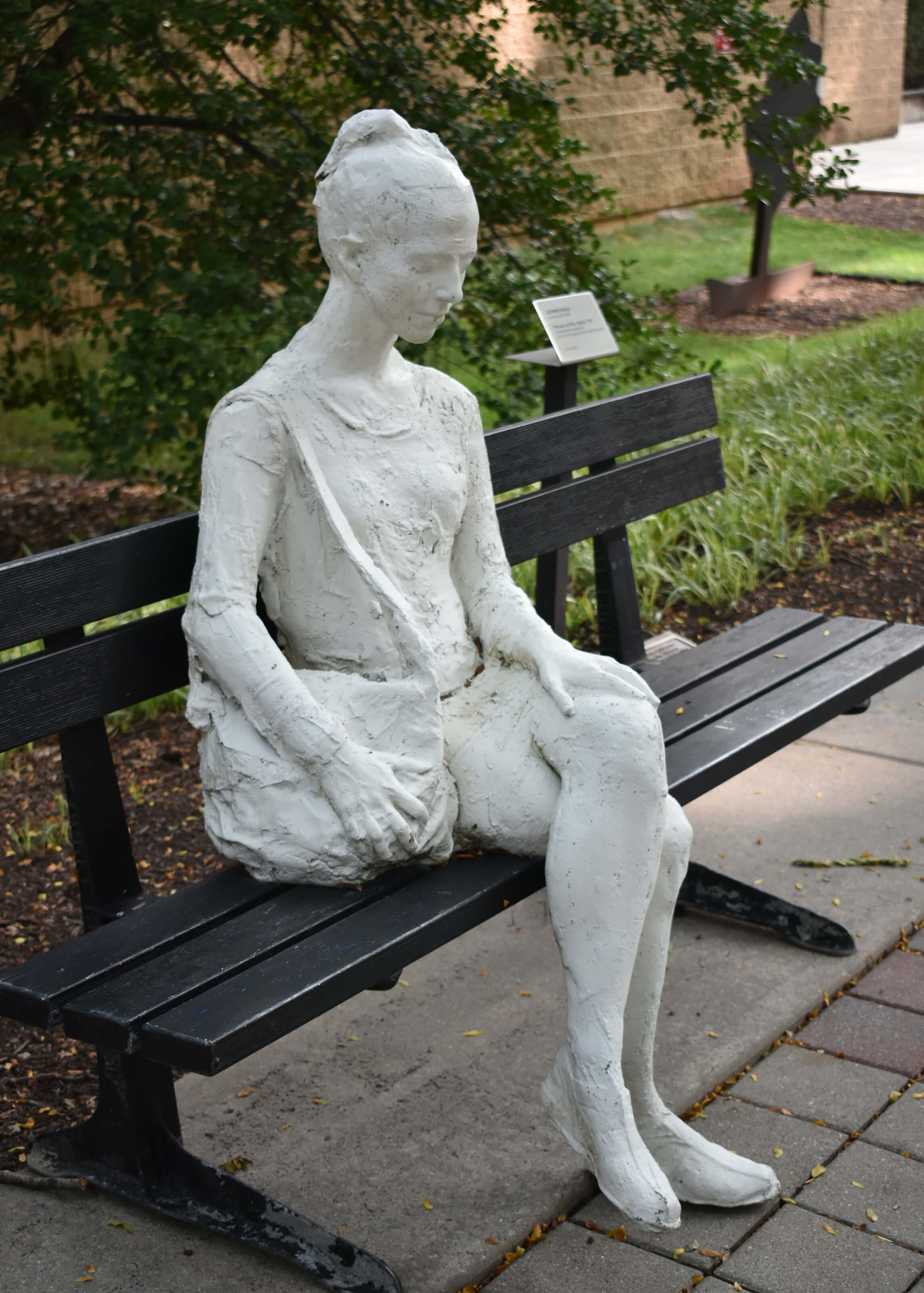 "Woman on a Park Bench" shows a light gray stone sculpture seated on a real park bench on Asa Packer campus.