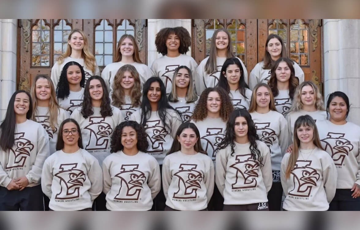 Women stand in front of historic building’s ornate doors, all wearing matching gray sweatshirts with Lehigh LHawk logos and smiling.