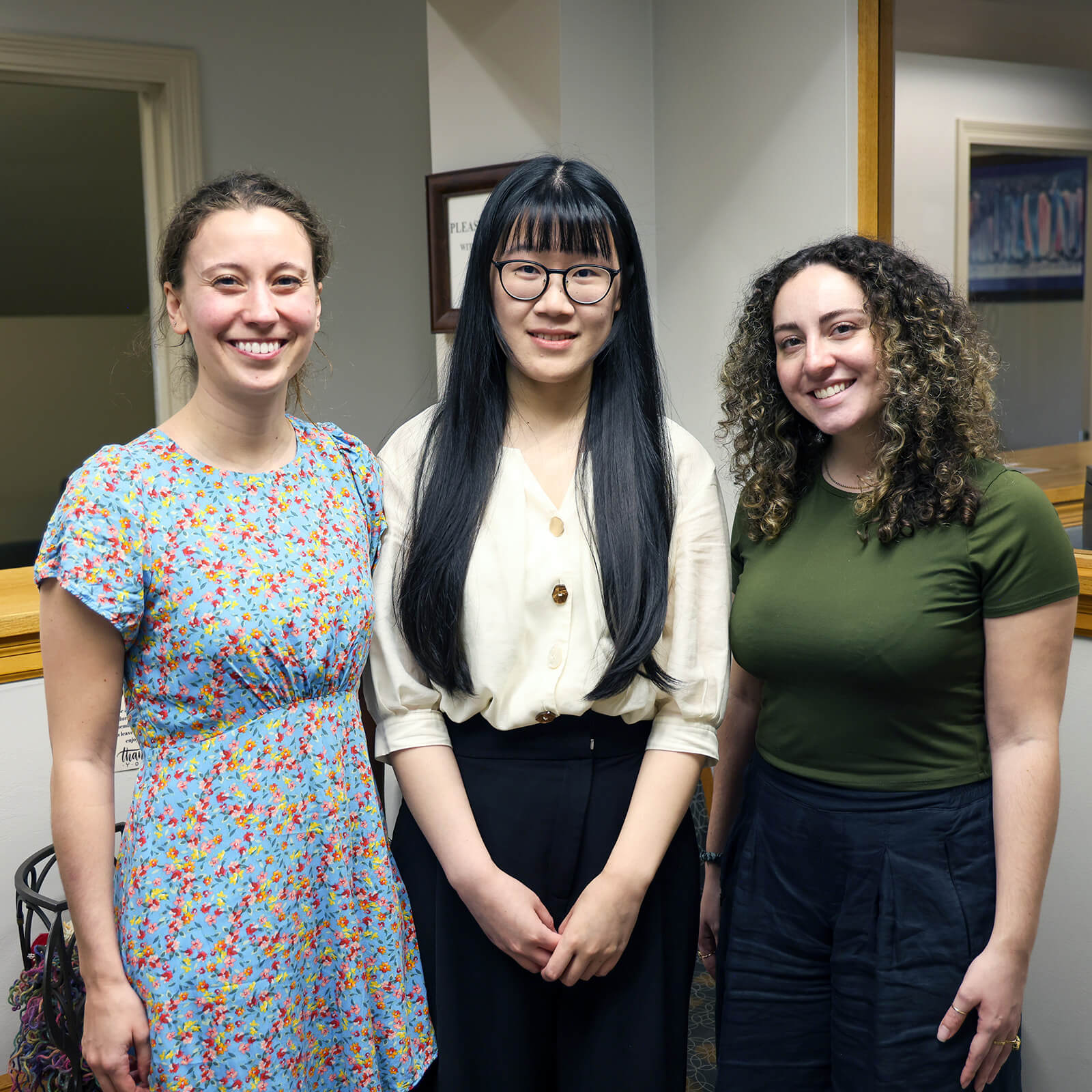 Three female doctoral students smile at the camera, posing in the UCPS offices.