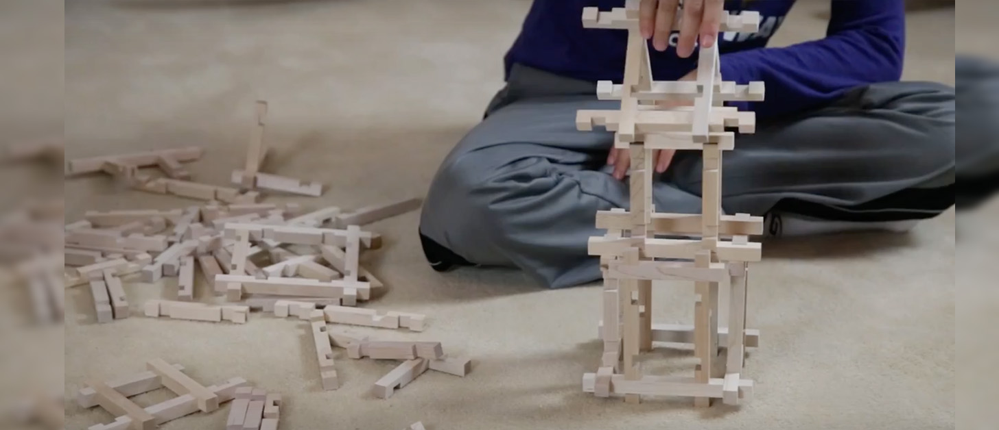 A close up a child's hands constructing notched wooden building sticks into a tower.