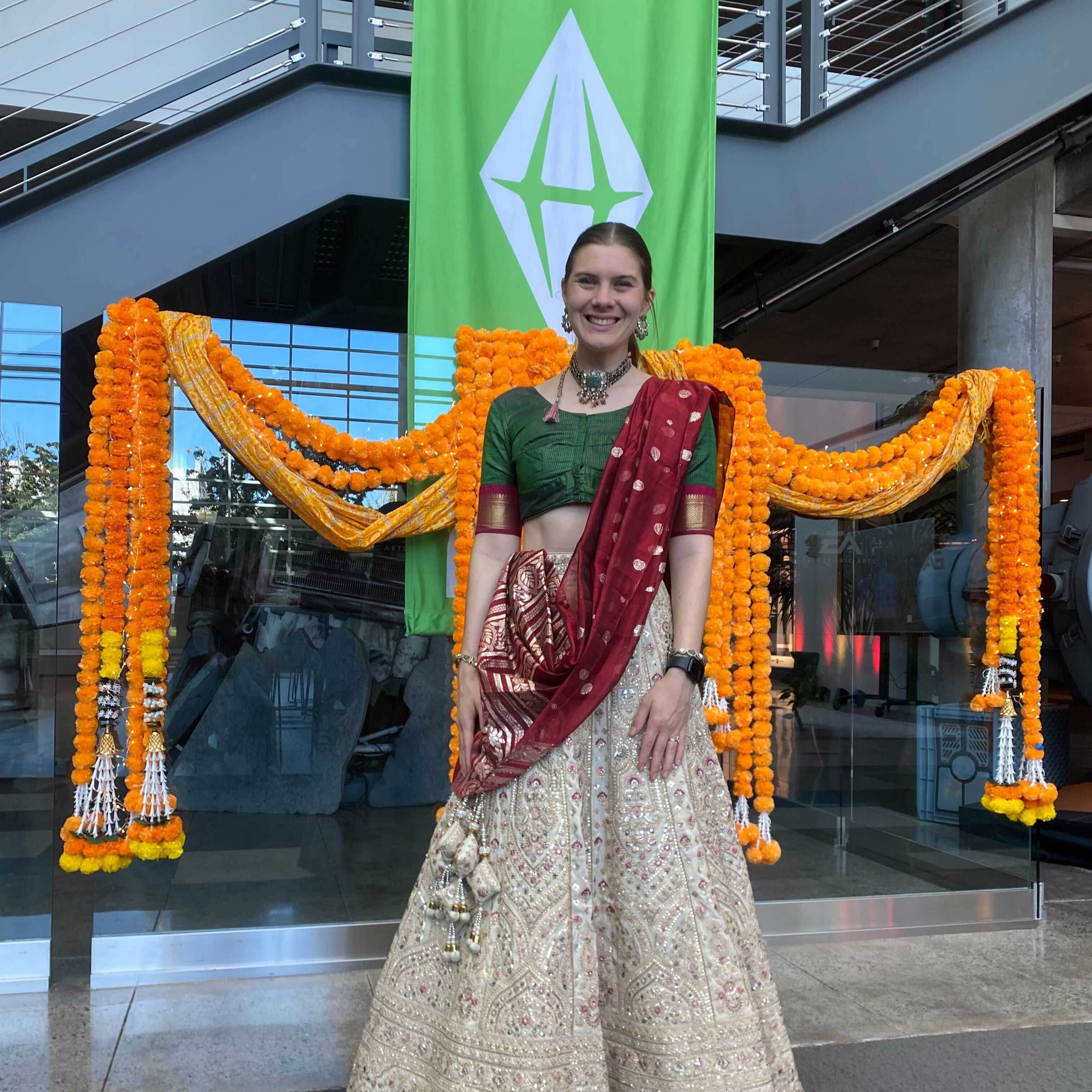 Alea wears a beaded, traditional Indian dress for Diwali and a sari. Behind her is an Electronic Arts banner with the Sims logo.