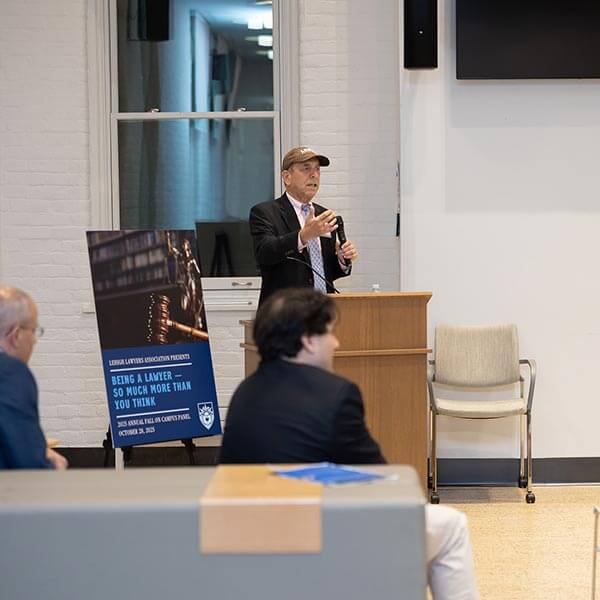 Barry Glickman moderates the panel while wearing a brown Lehigh hat