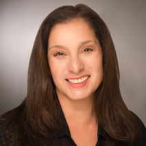 Beth smiles and wears a black, business casual top. Her dark brown hair falls just past her shoulders. 