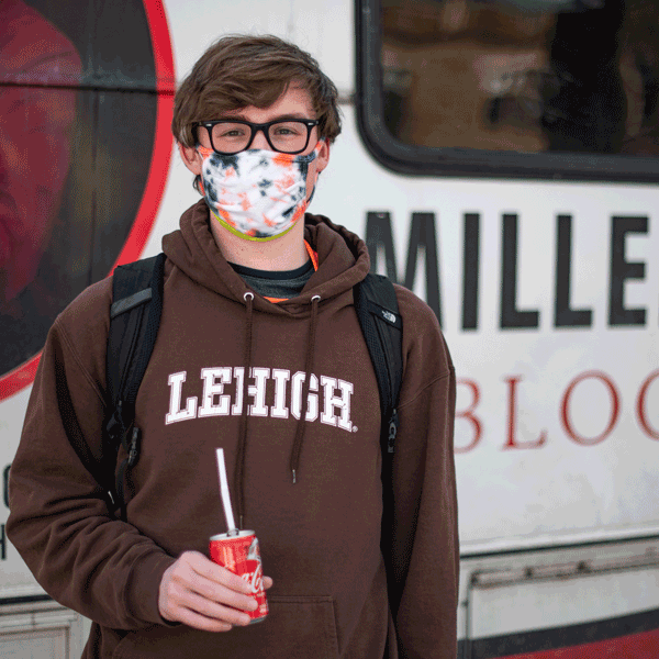 A student standing in front of a blood drive truck wearing a brown Lehigh University hoodie and a tie dyed mask covering his mouth