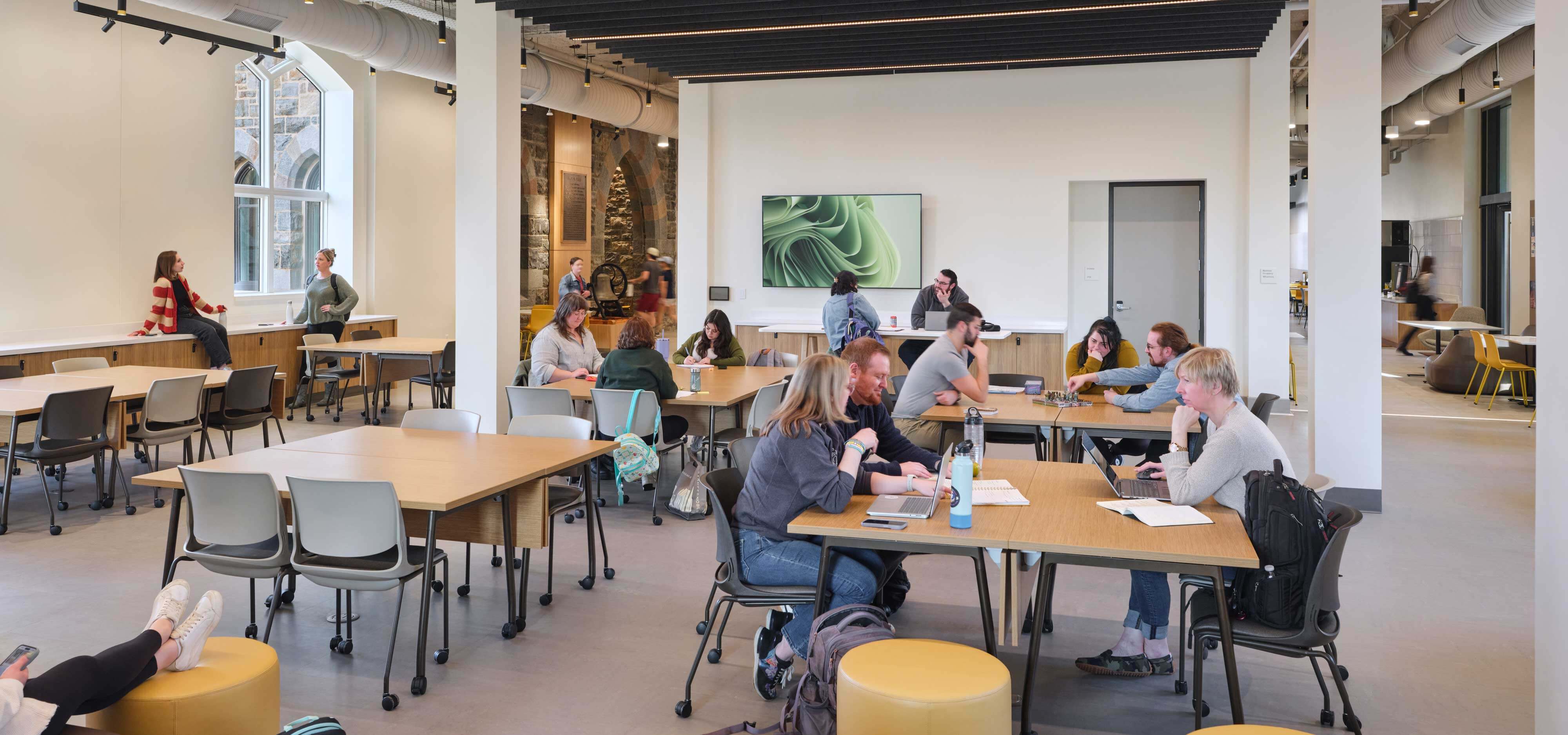 People sit in groups at varying tables in the Club Hub.
