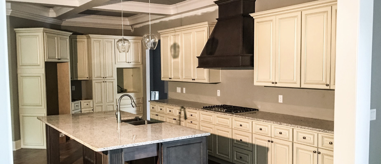 A large kitchen with white cabinets, white marble counters, black stove, hanging glass pendant lights, and island with silver sink