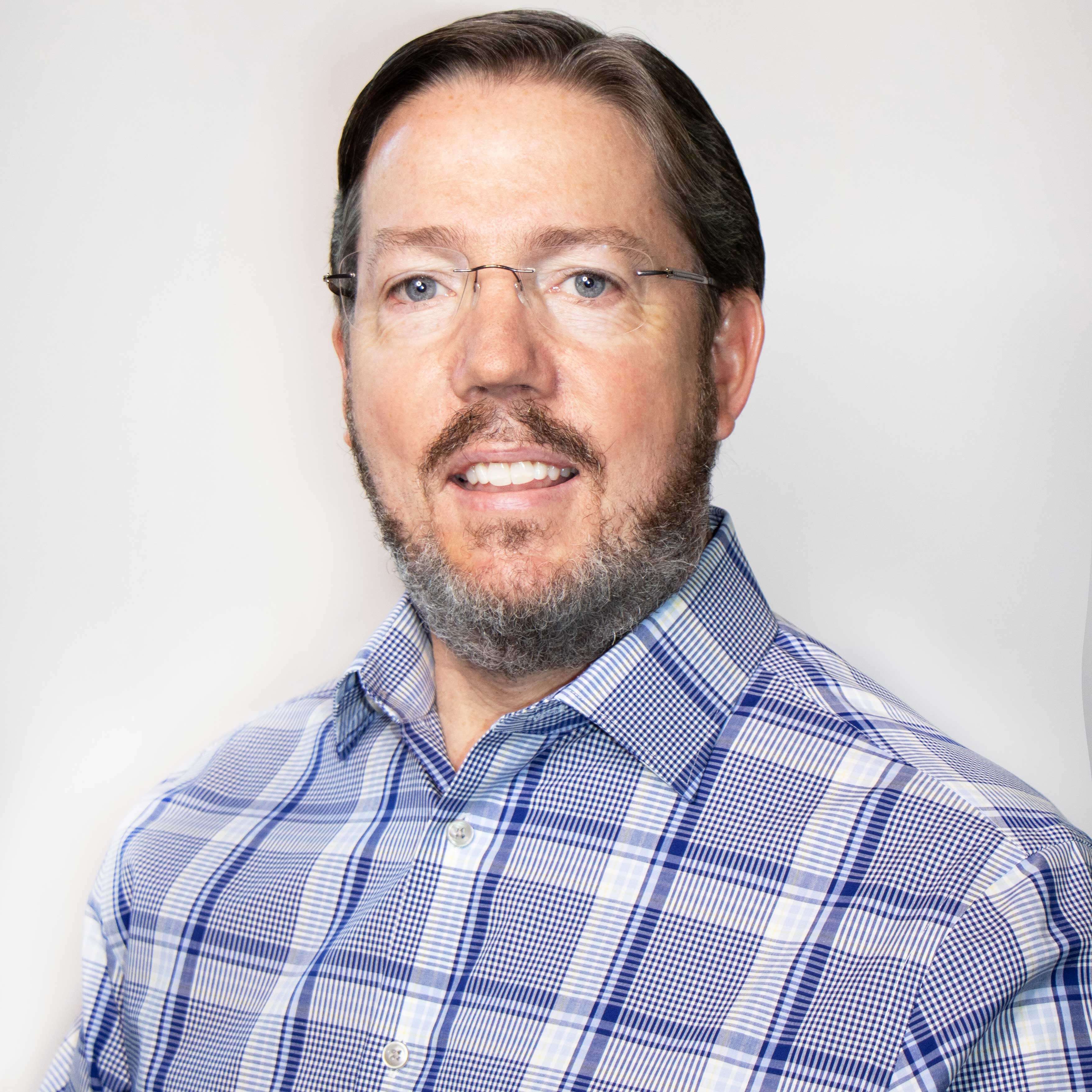 Edward wears a white and blue plaid button down and glasses. The portrait lighting is bright and crisp. He smiles.