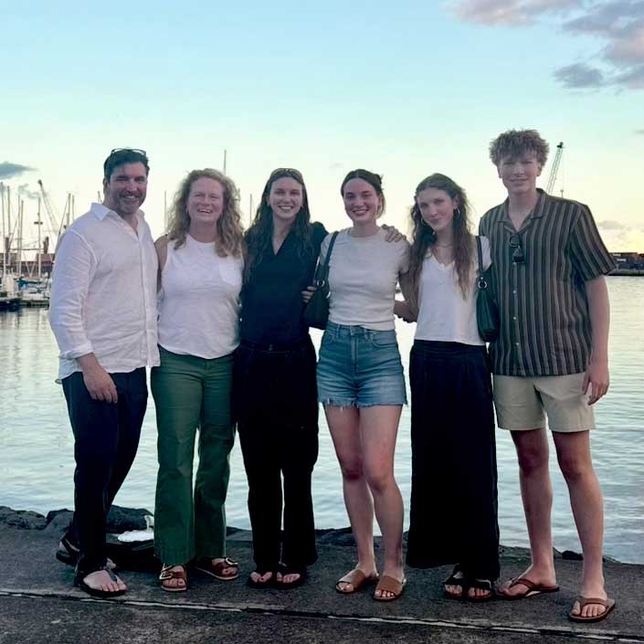 Bridget with her husband and family and vacation. Behind them, there is a lake and several boats.