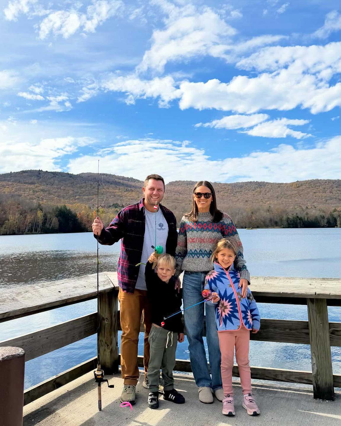 Danielle and her family pose in front of a lake on a sunny day. Her husband and children proudly hold up fishing poles and grin. 
