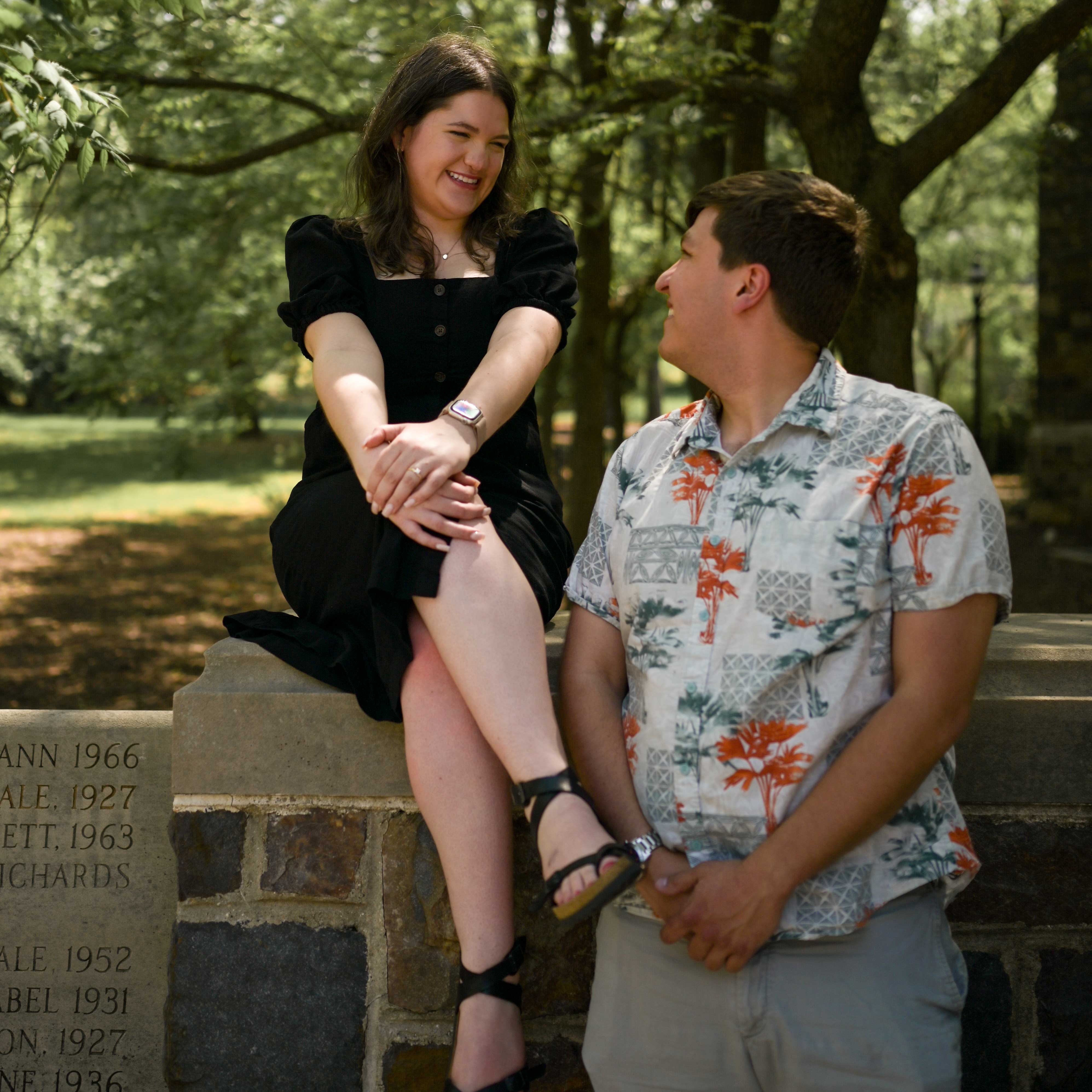 Janice sits on a stone edge outside of Packer Memorial Church in a black dress. Eddie looks back at her and smiles. 