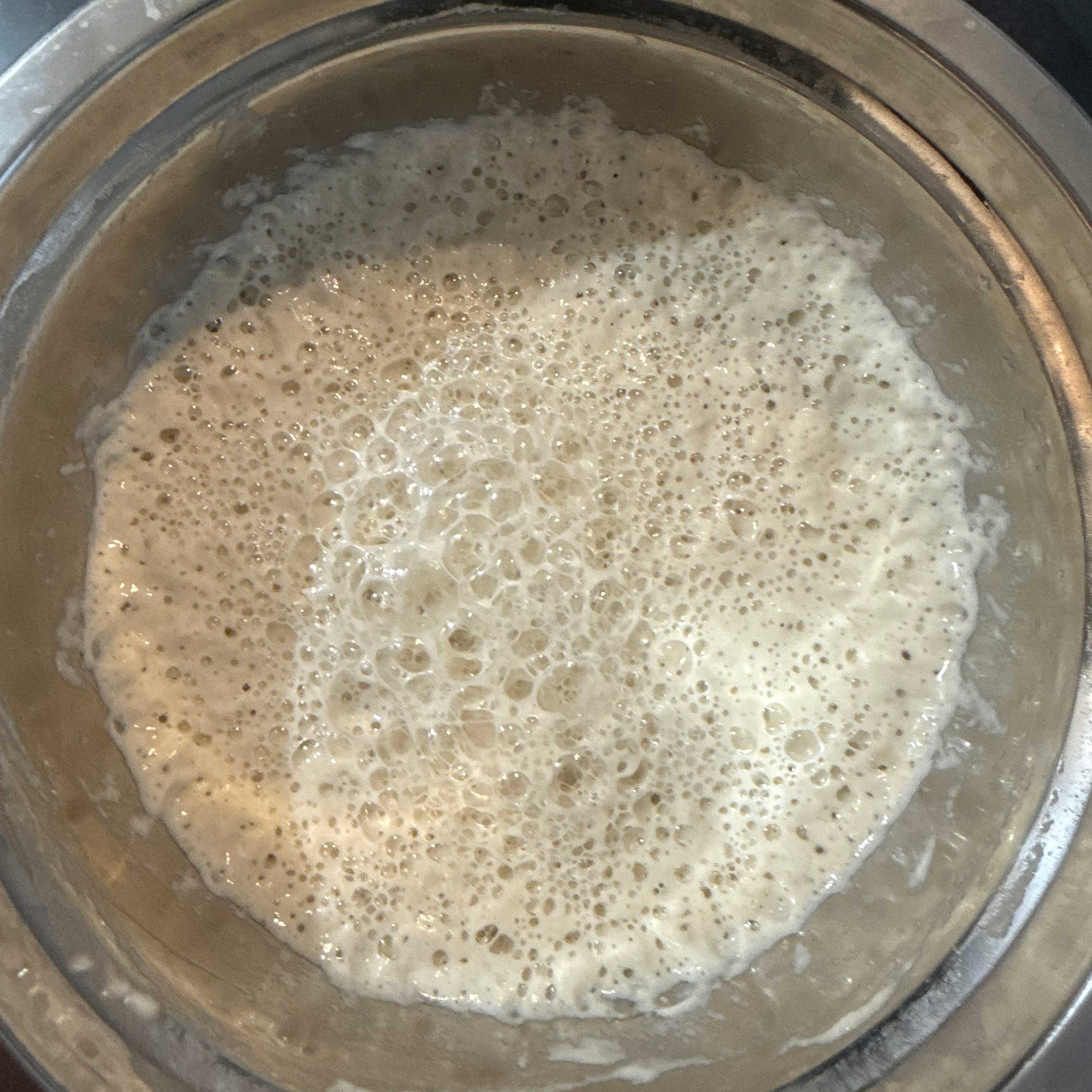 A bubbly, active sourdough starter inside a jar. The starter is a light beige color with a layer of foam near its middle. 
