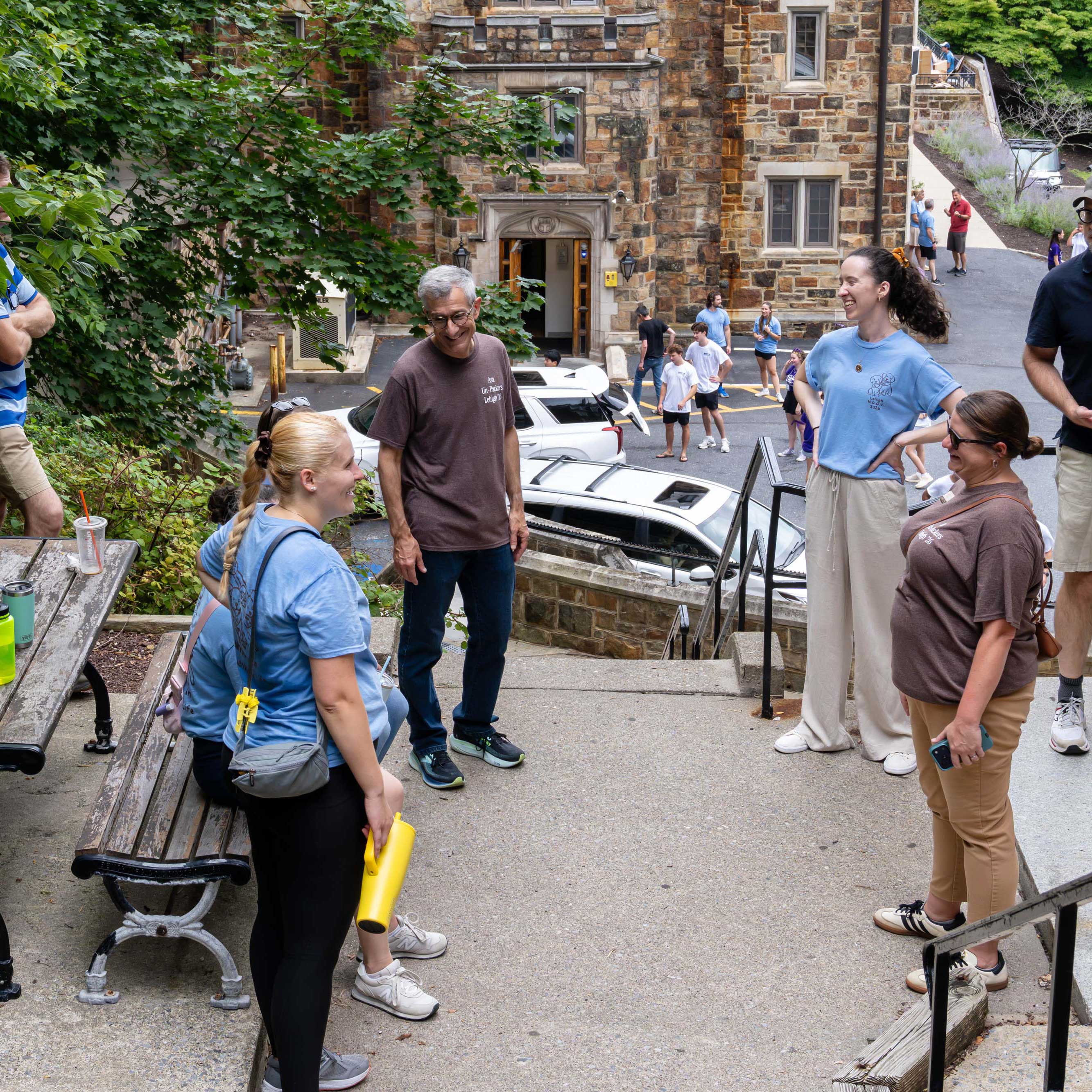 Volunteers in brown and light blue shirts chat outside a dorm during move-in and smile.