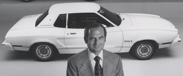 Lee Iacocca in front of a white 1964 Ford Mustang