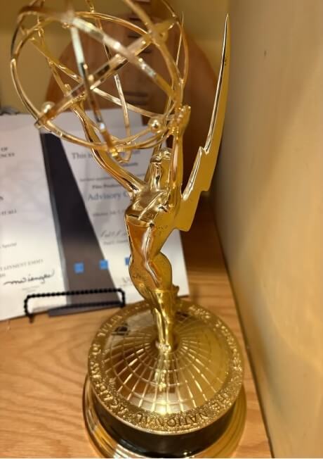 Beth's golden Emmy sits on her bookshelf in front of several other awards.