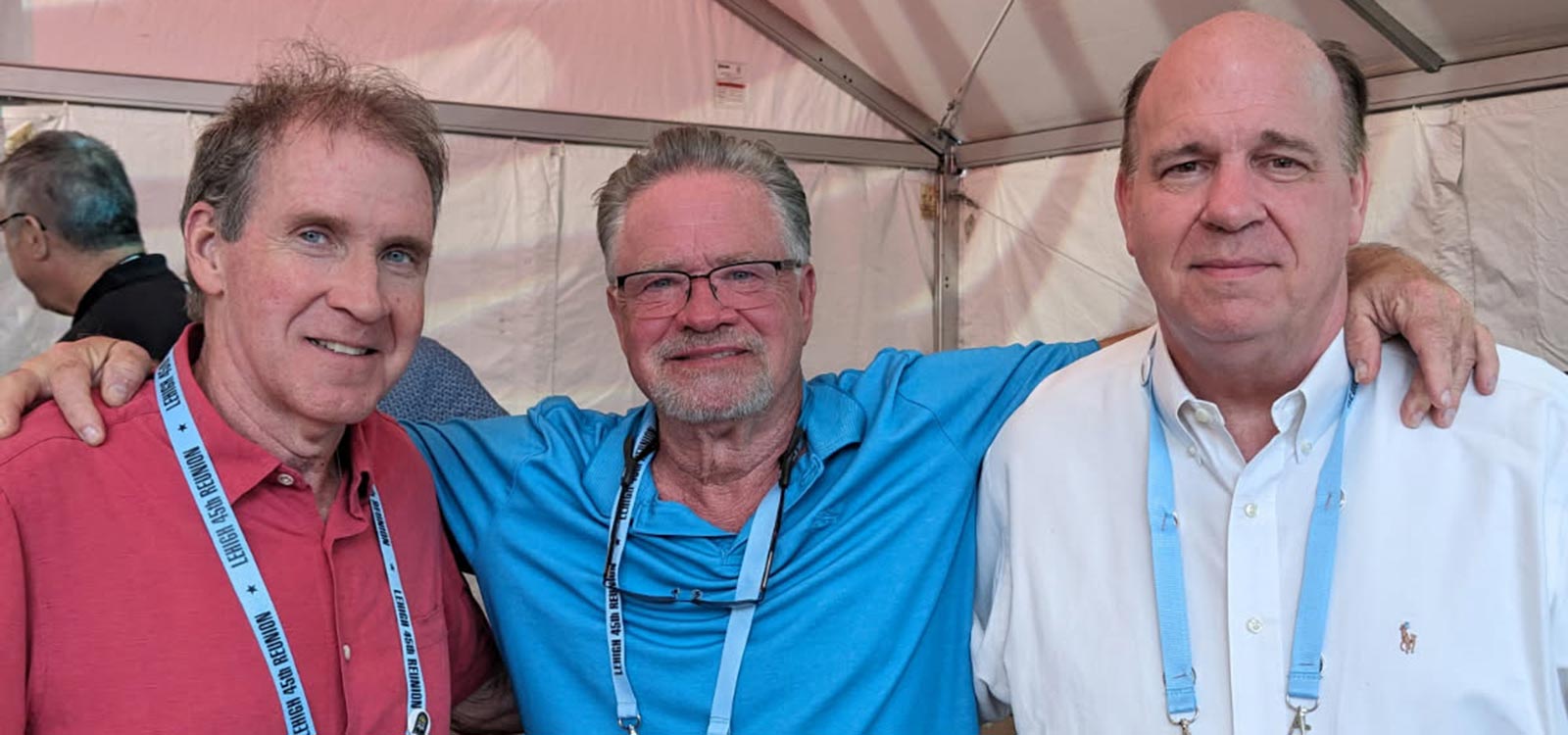 Jim, Dave, and Pete stand under a tent at their college reunion; David has an arm around both men.