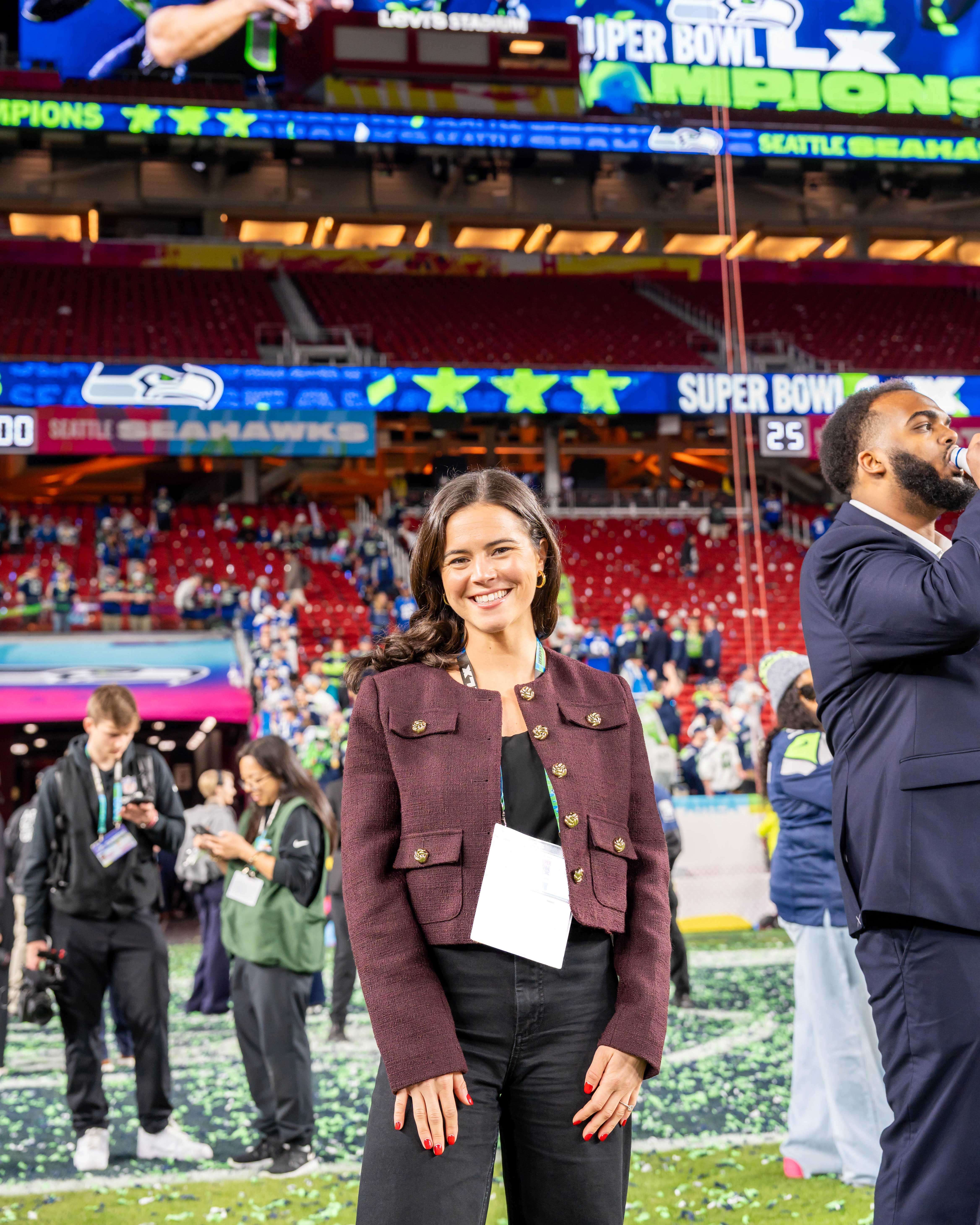 Kendall smiles as she stands on the Super Bowl field; confetti is strewn on the turf. She wears a tweed, maroon blazer.