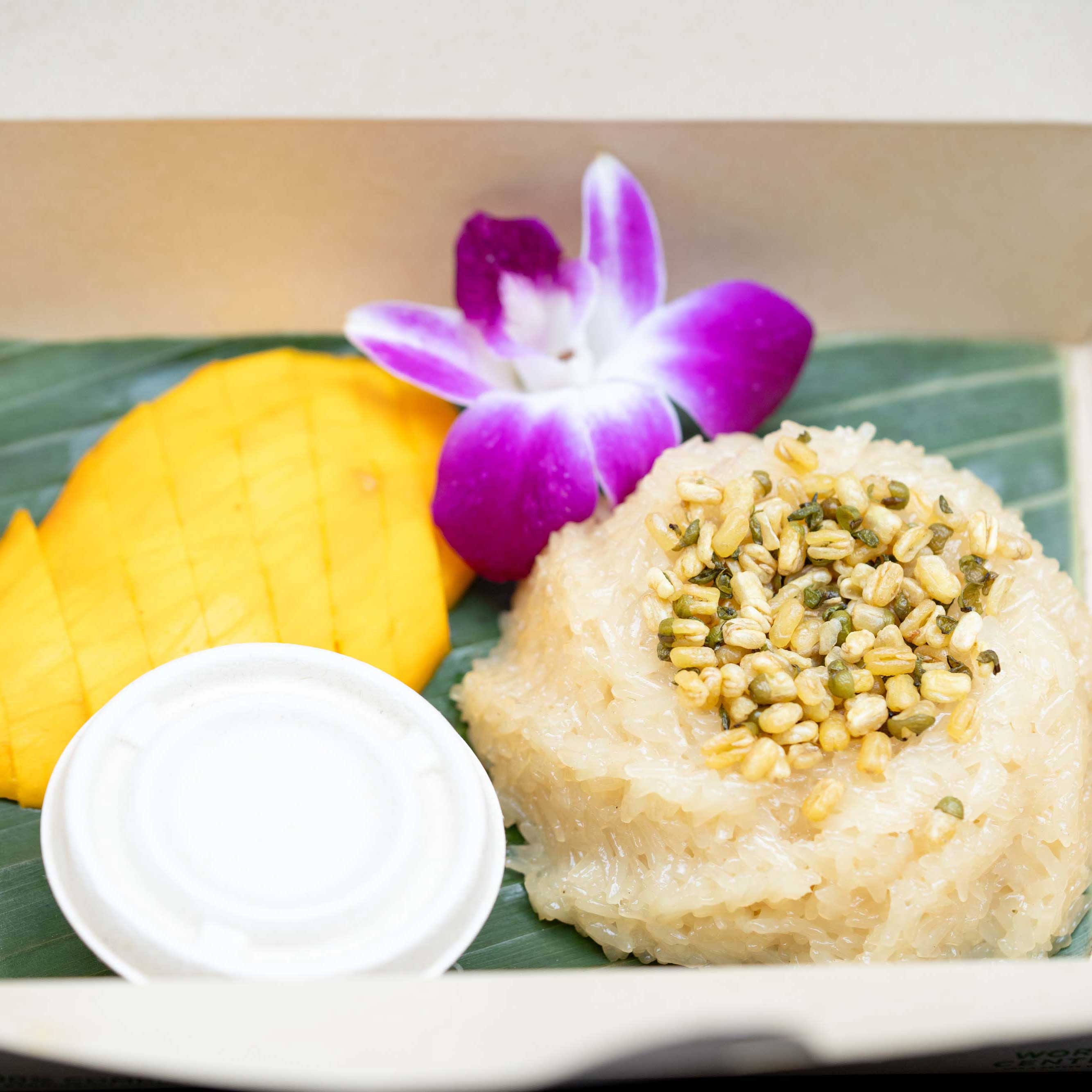 A scoop of sticky rice alongside vibrant, ripe mango and an orchid flower. 