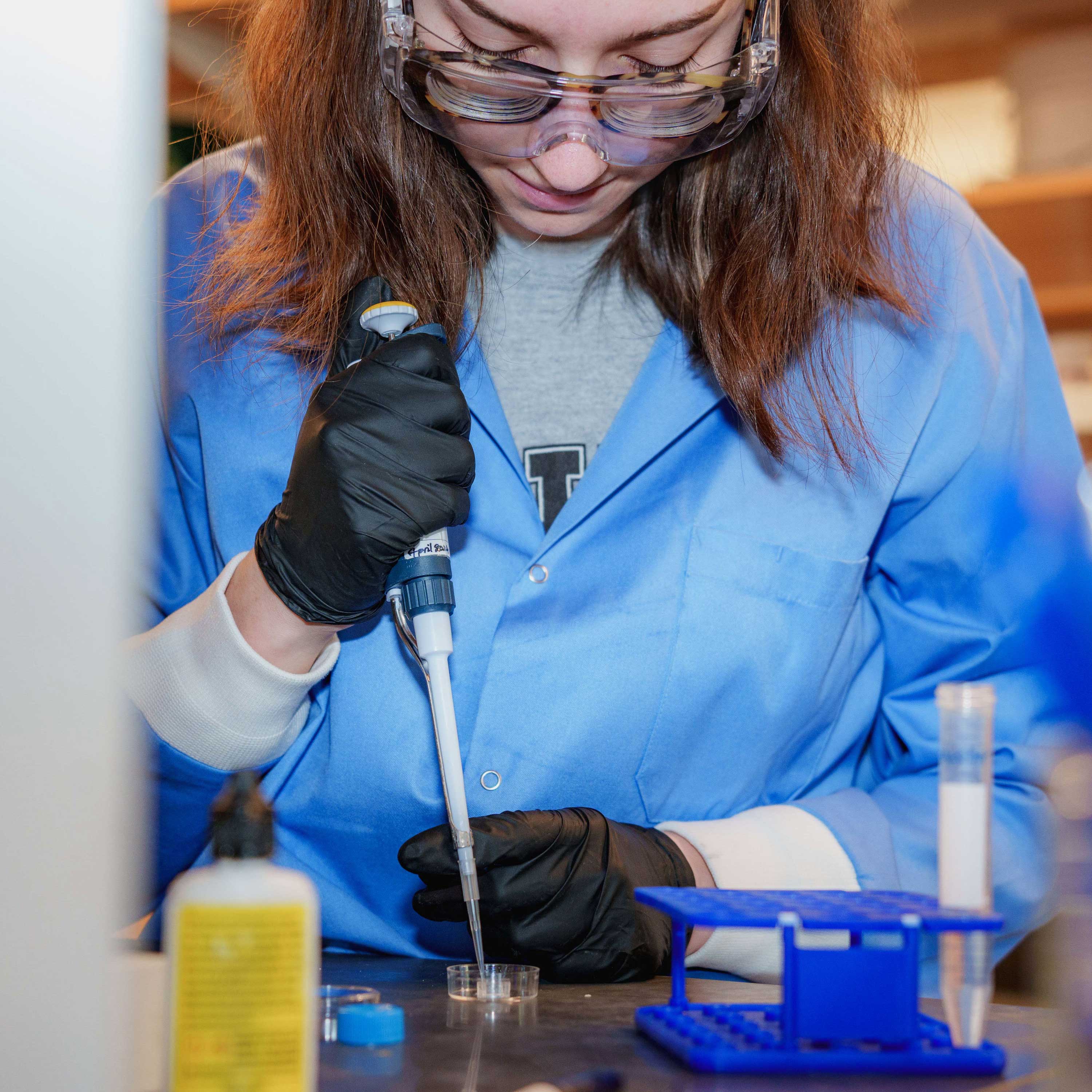 A student in a blue lab coat performs research.