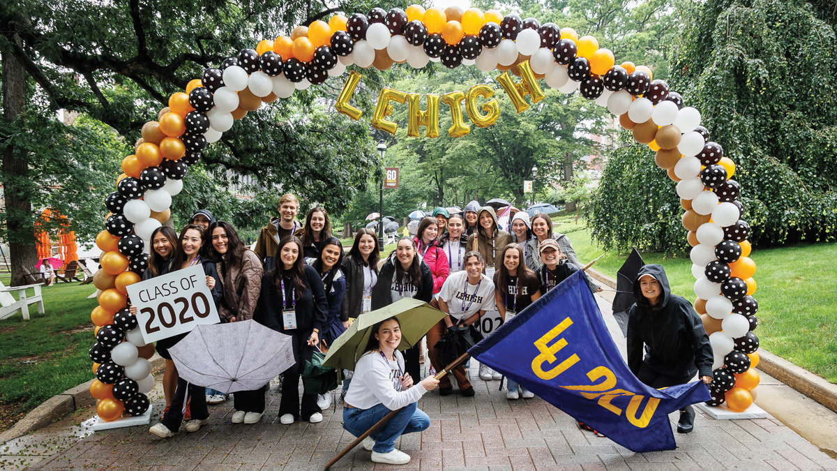 A group of people pose for a group photo while outside, under a balloon arch.