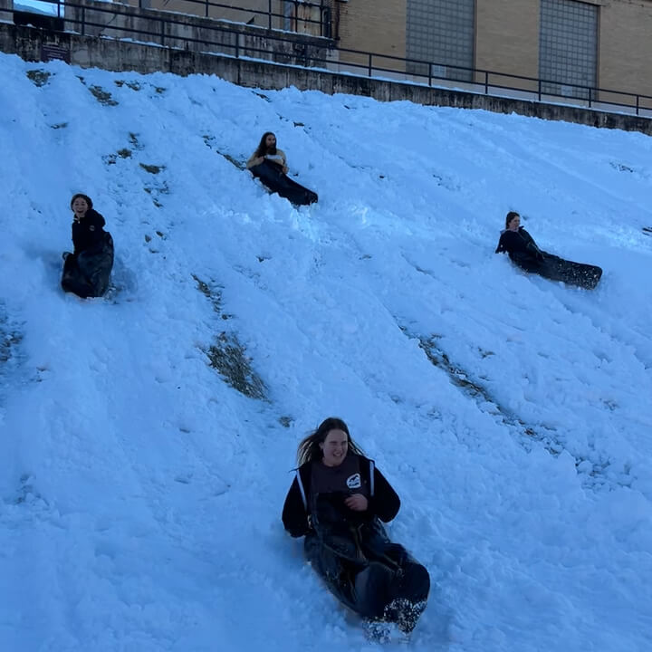 Gabby and her friends sled down a hill on campus on a thick layer of snowfall. They smile and laugh.