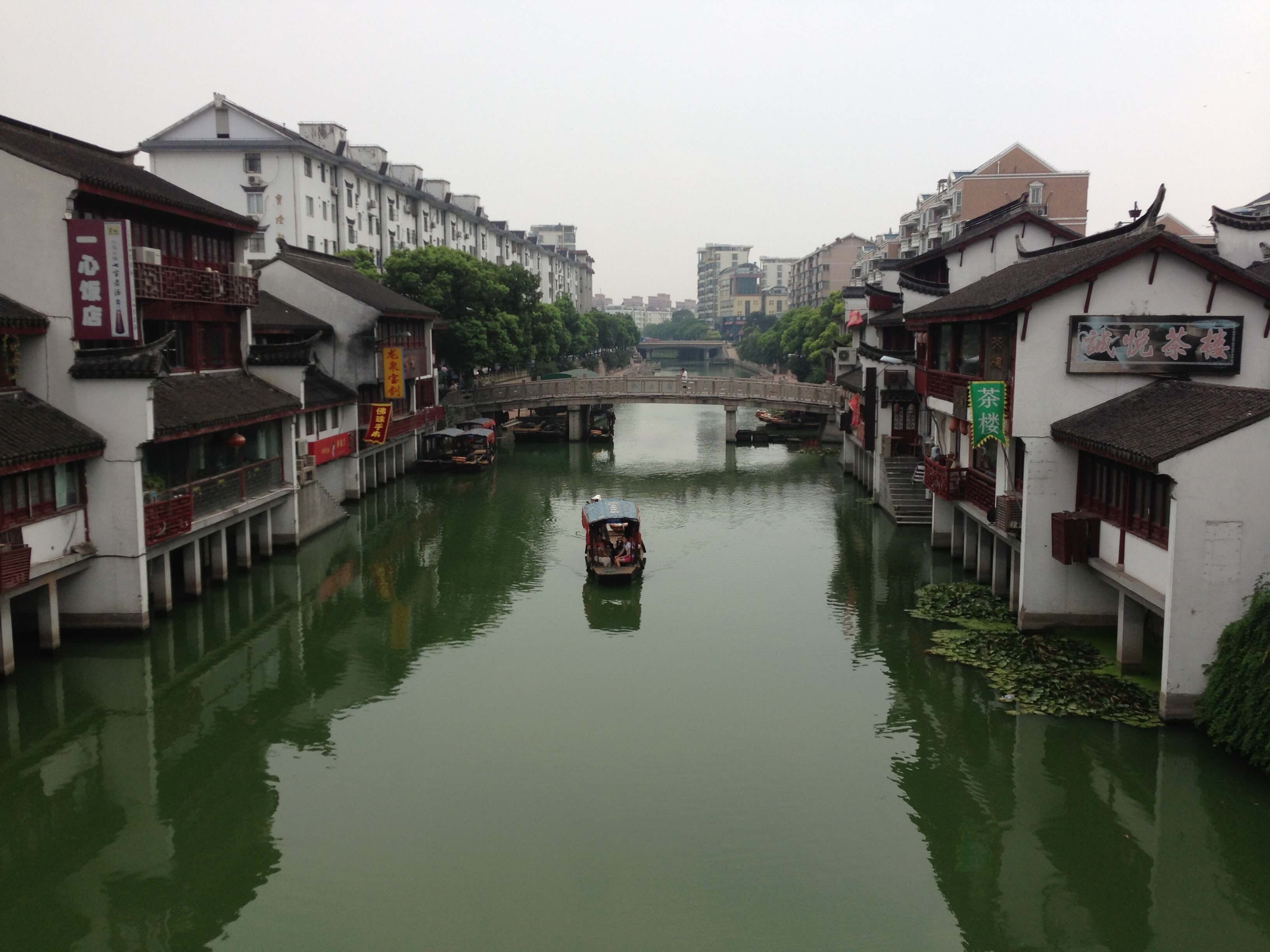 A gondola rides through a canal in Zhujiajiao. The water is a deep green color, and white buildings frame the photo on both sides.