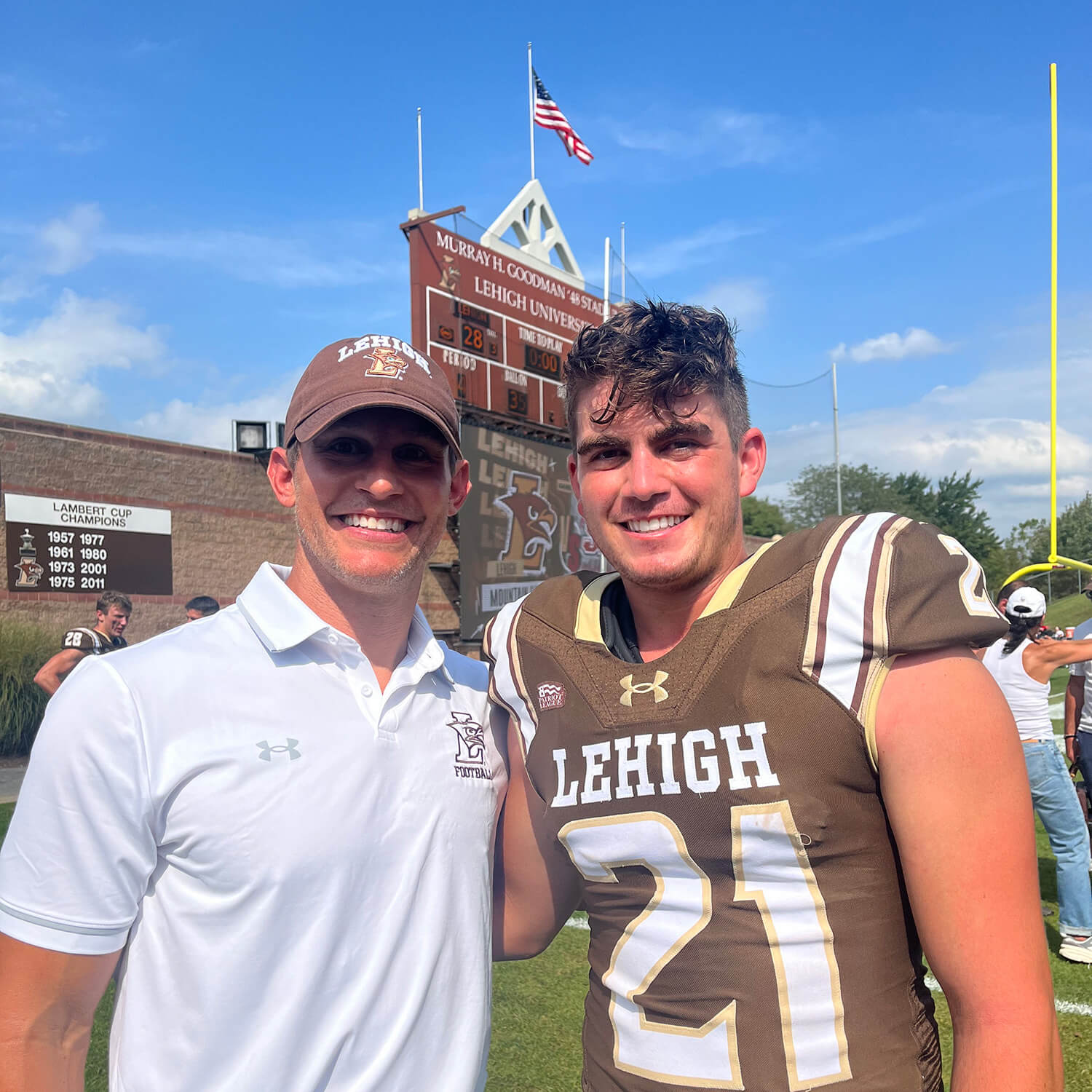 Canaan Kimball and Coach Kevin Cahill smile in front of the scoreboard at Goodman Stadium