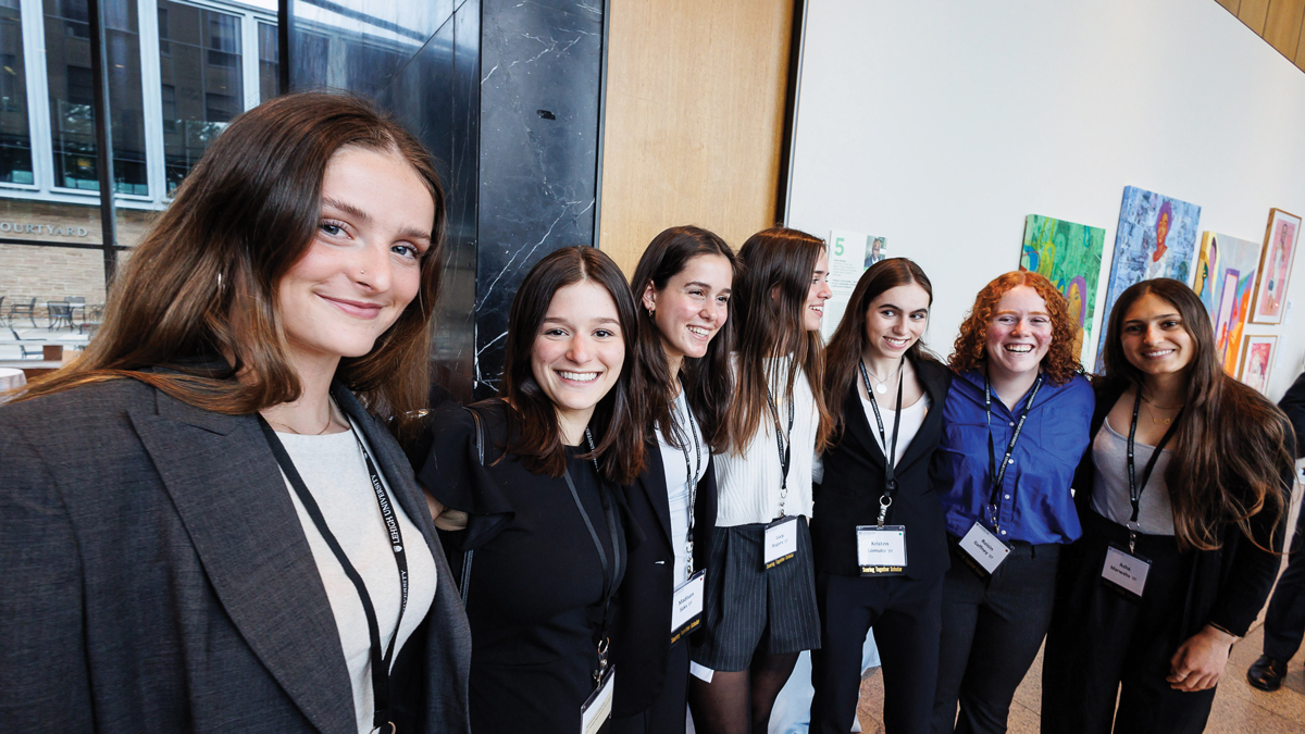 A groups of women embrace for a group photo during an art gallery event.