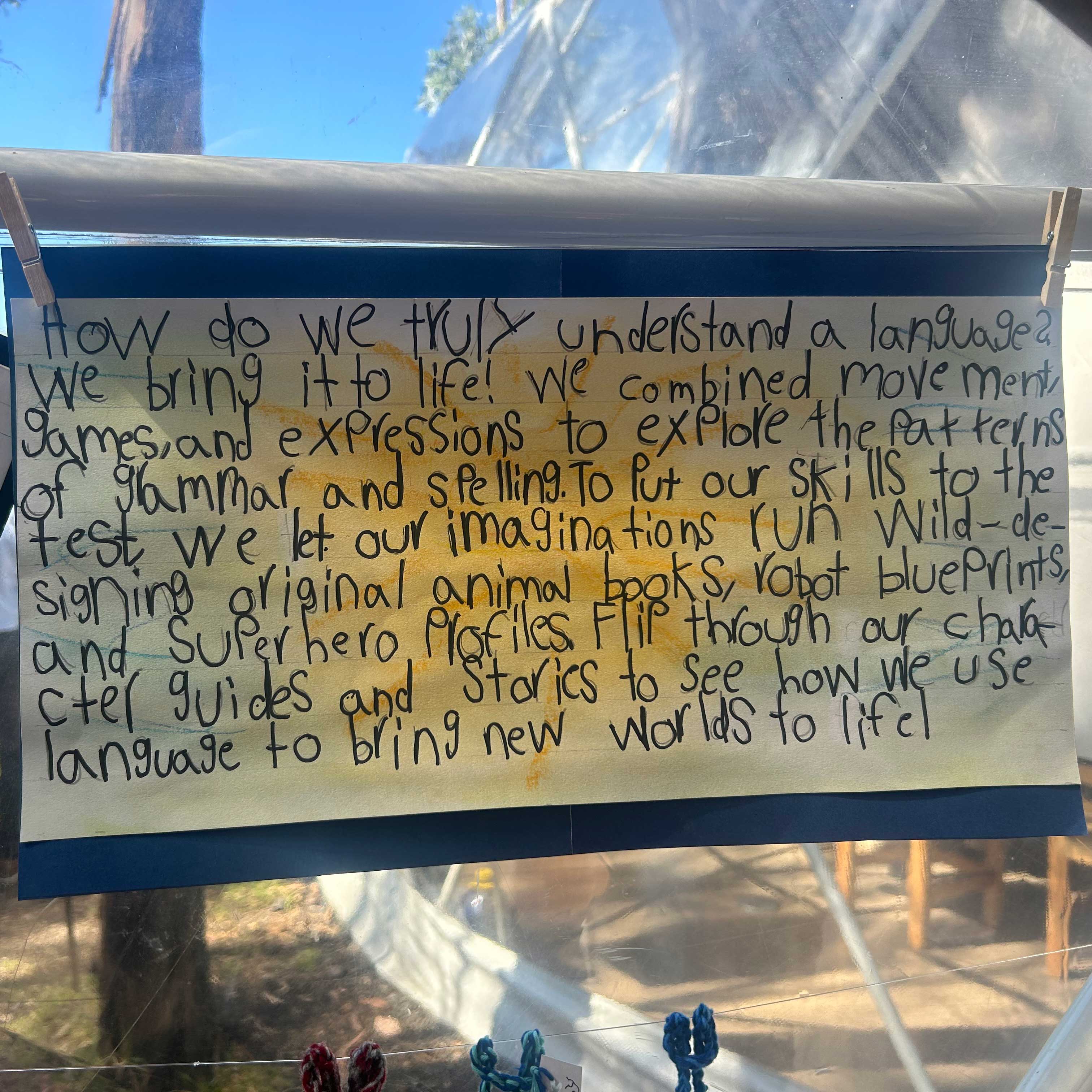 A student notecard hangs from clothing pins on a window.