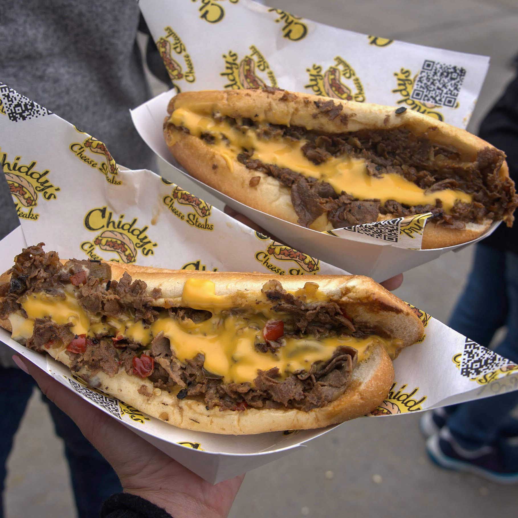 Two large cheesesteaks with visible whiz, steak, and red sauce.