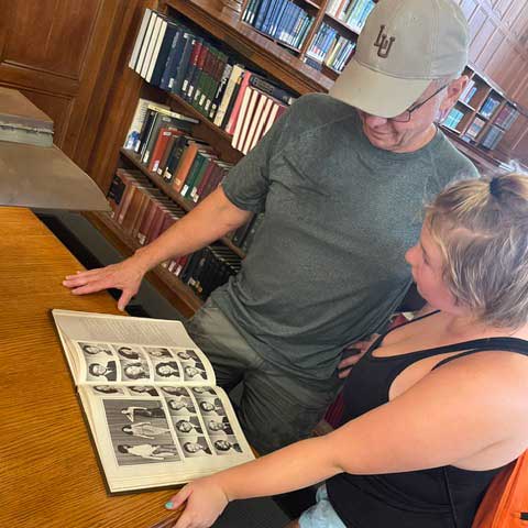Gillian and Glenn stand in Linderman Library and look down at the 1980 yearbook images.