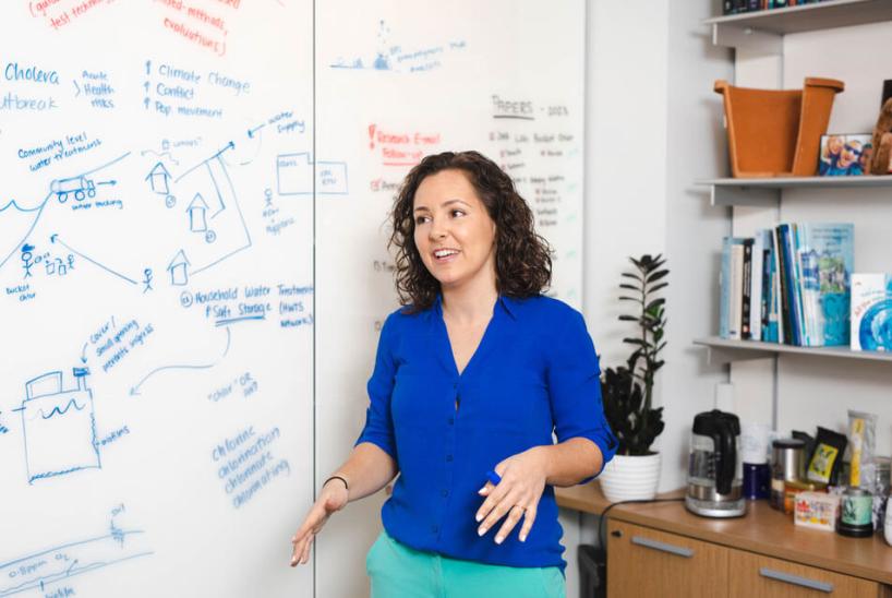 A woman standing in front of a whiteboard with drawings and diagrams.