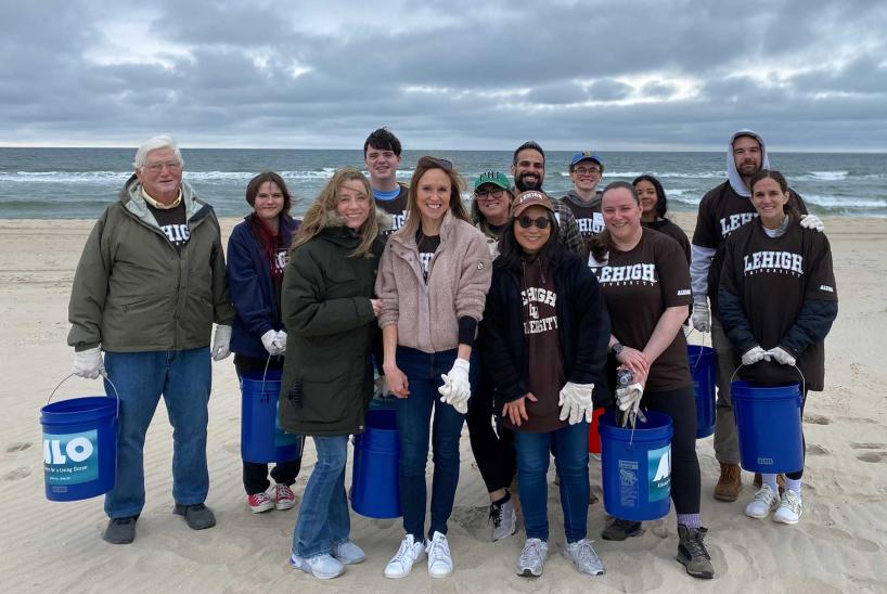 Alumni and friends standing on a beach, wearing coats and carrying buckets.