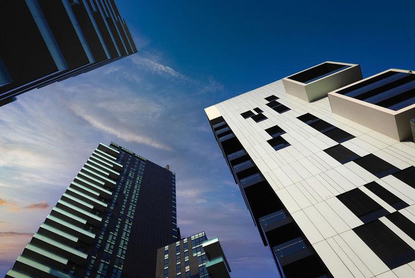 Modern high-rise buildings with geometric designs are seen from a low angle against a deep blue sky with wispy clouds at sunset.