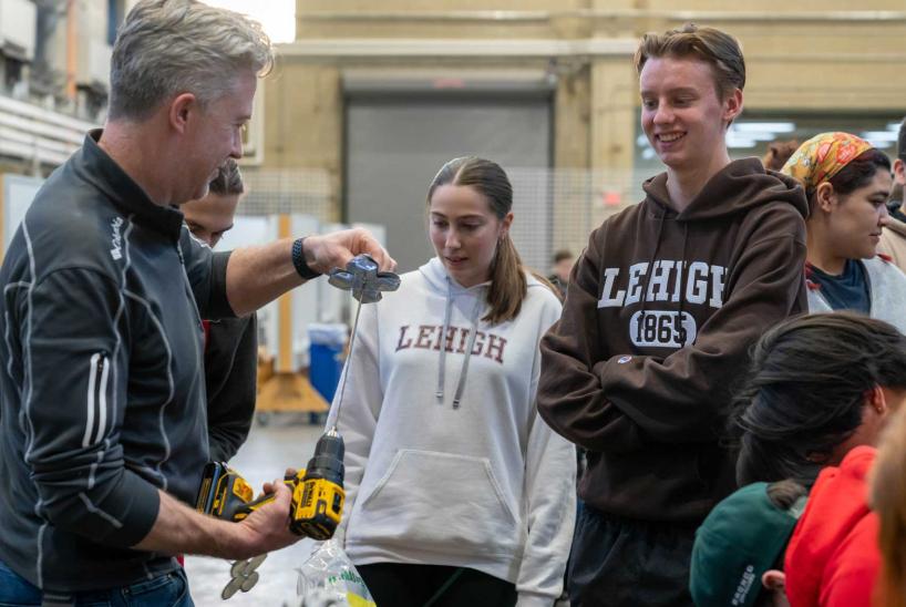 Two students watch as a professor creates a metal flower.